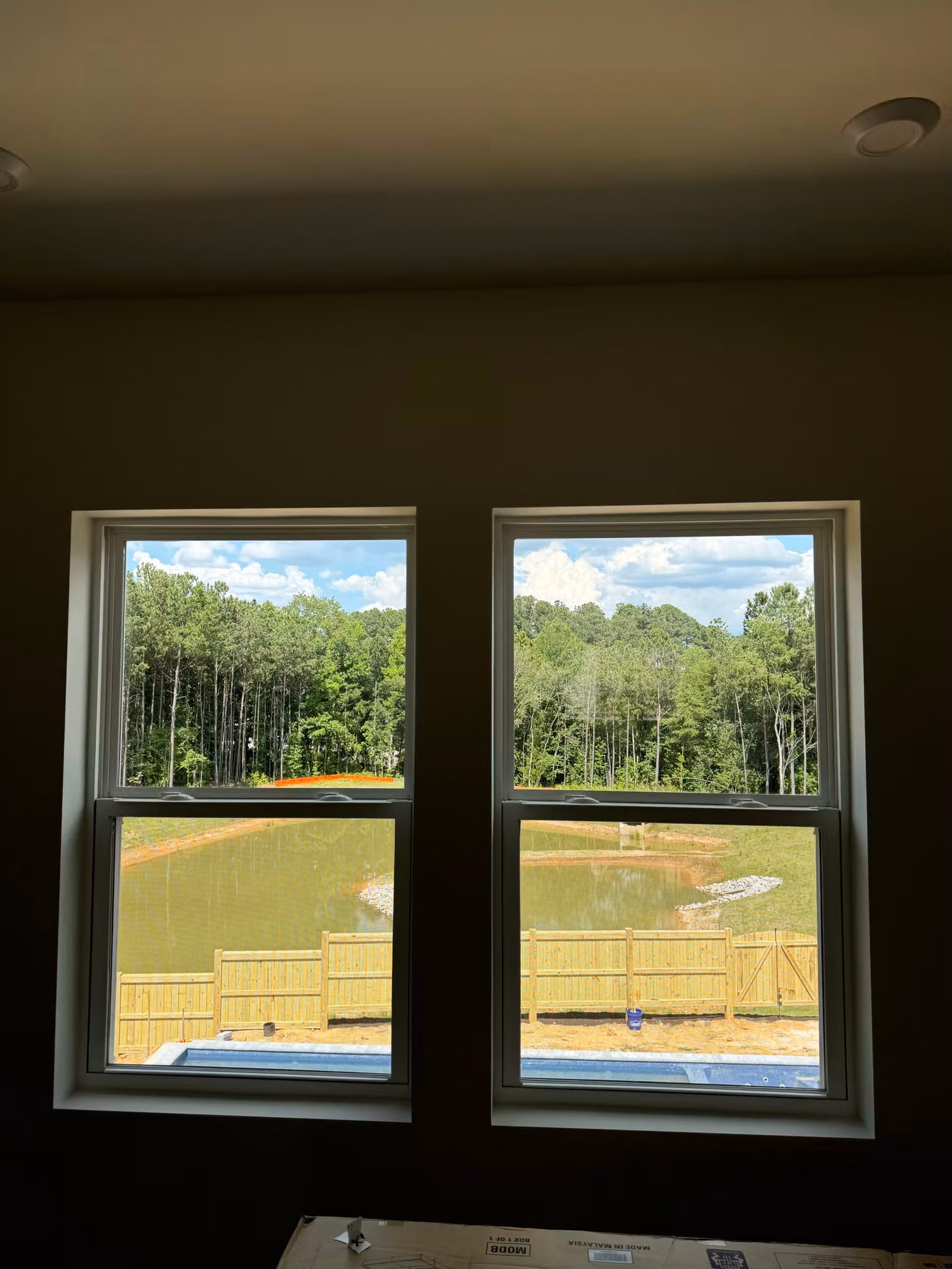 Pair of double-hung home windows with window film overlooking a backyard pond and wooded tree line.
