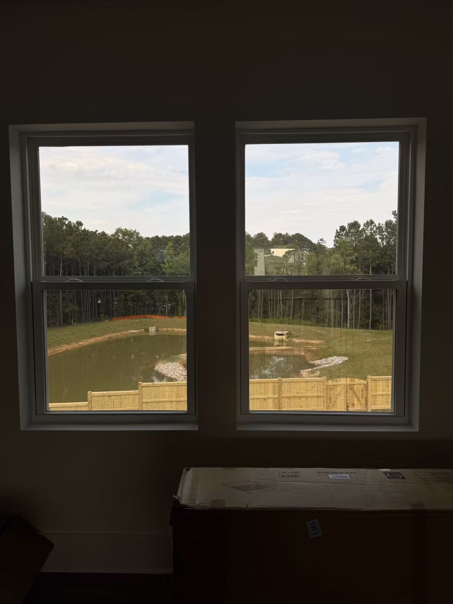 Two double-hung windows treated with window film overlooking a backyard pond and wooden fence.