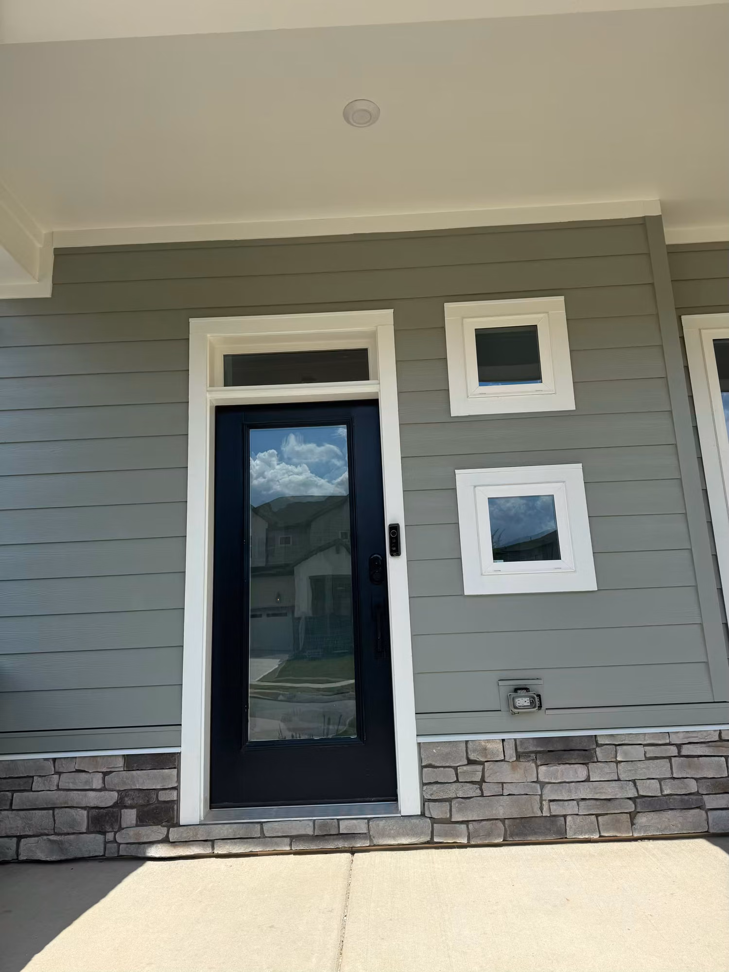 Full-glass front entry door with transom and square sidelight windows showing fresh window film on a home.