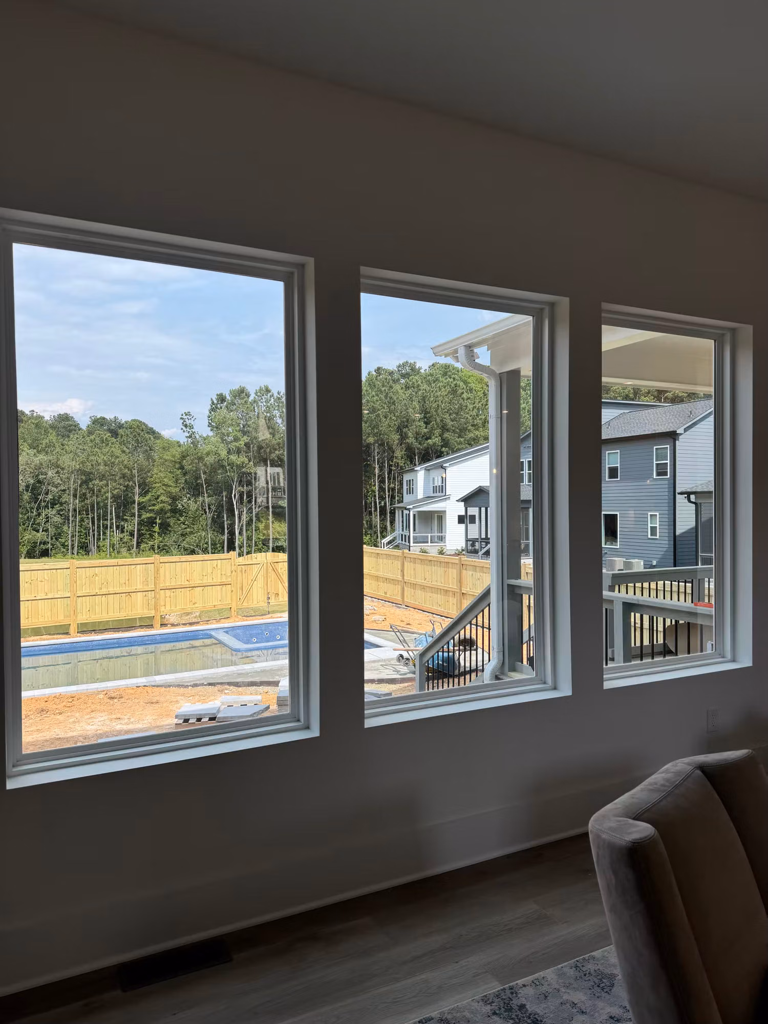 Three large living room picture windows overlooking a backyard pool and neighboring two-story homes.