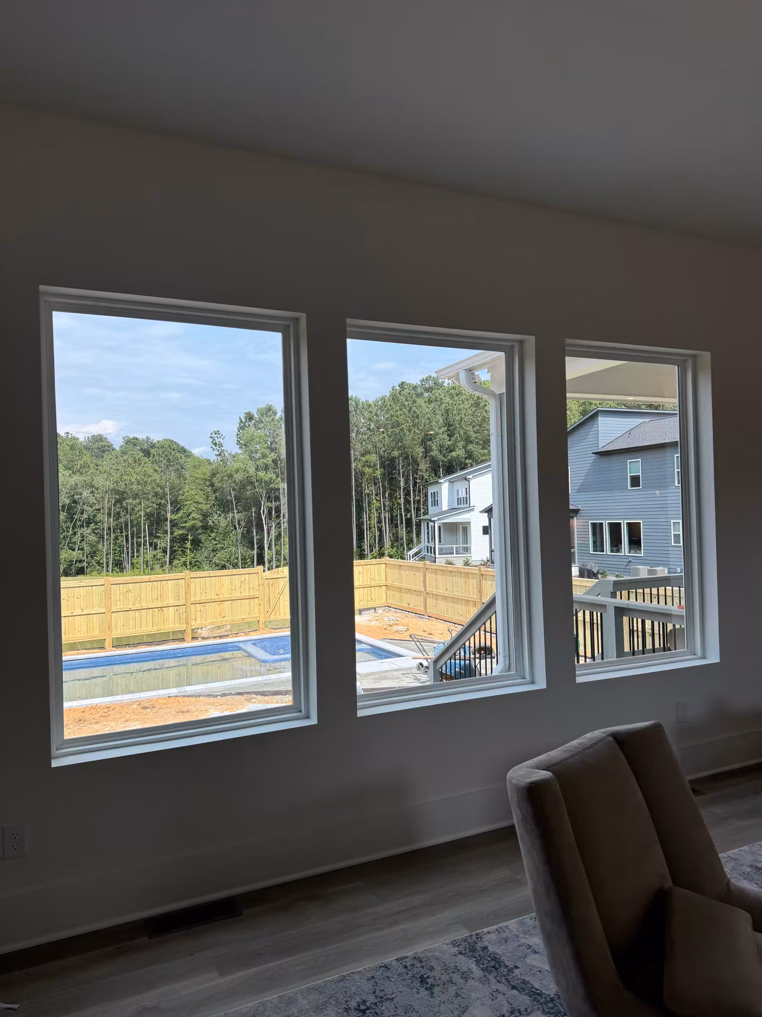 A row of three living room windows framing a view of the backyard pool and surrounding tree line.