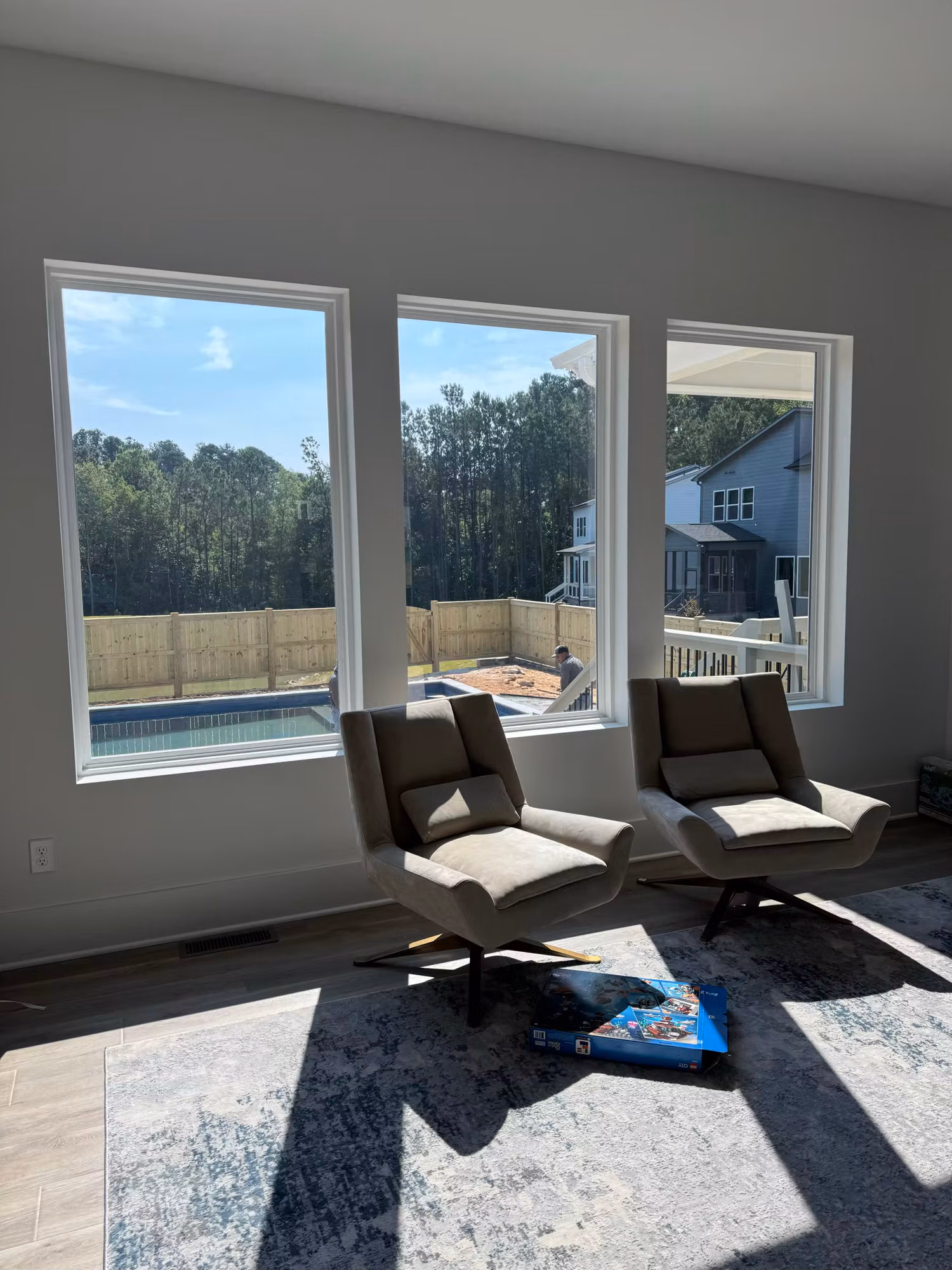 Three large living room windows with window film overlooking a backyard pool, with accent chairs in the foreground.