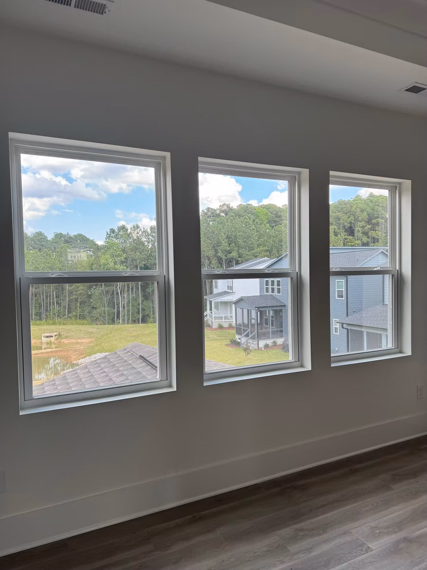 Empty room with three tall double-hung windows showing tinted glass and a view of nearby houses and trees.