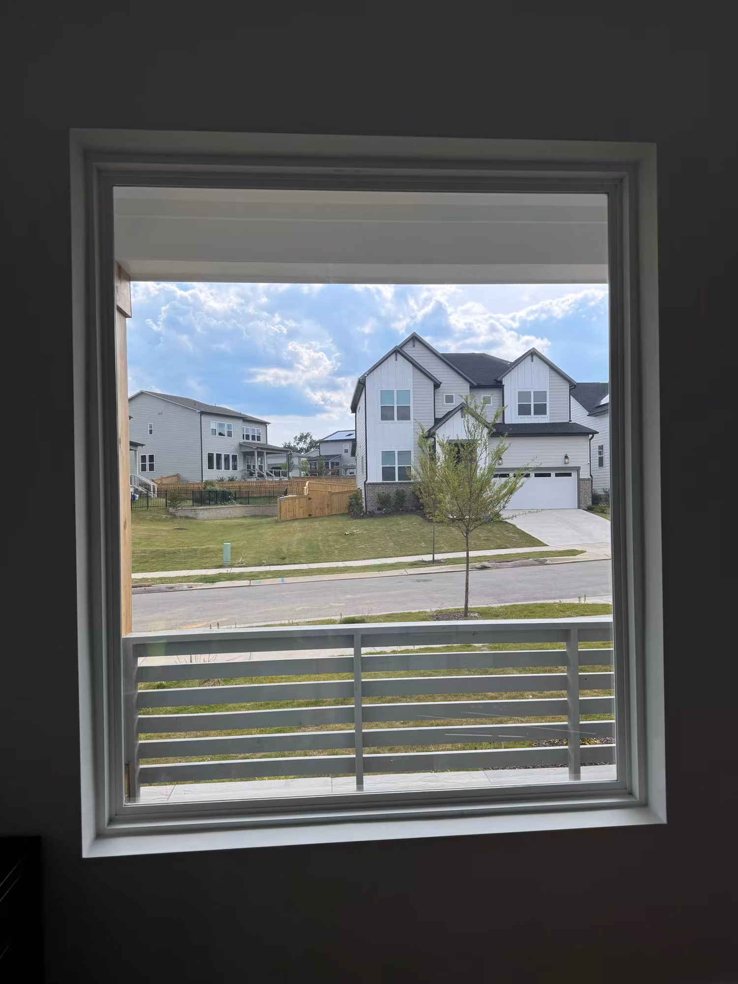 A large upstairs picture window overlooking a residential street and neighboring two-story homes.