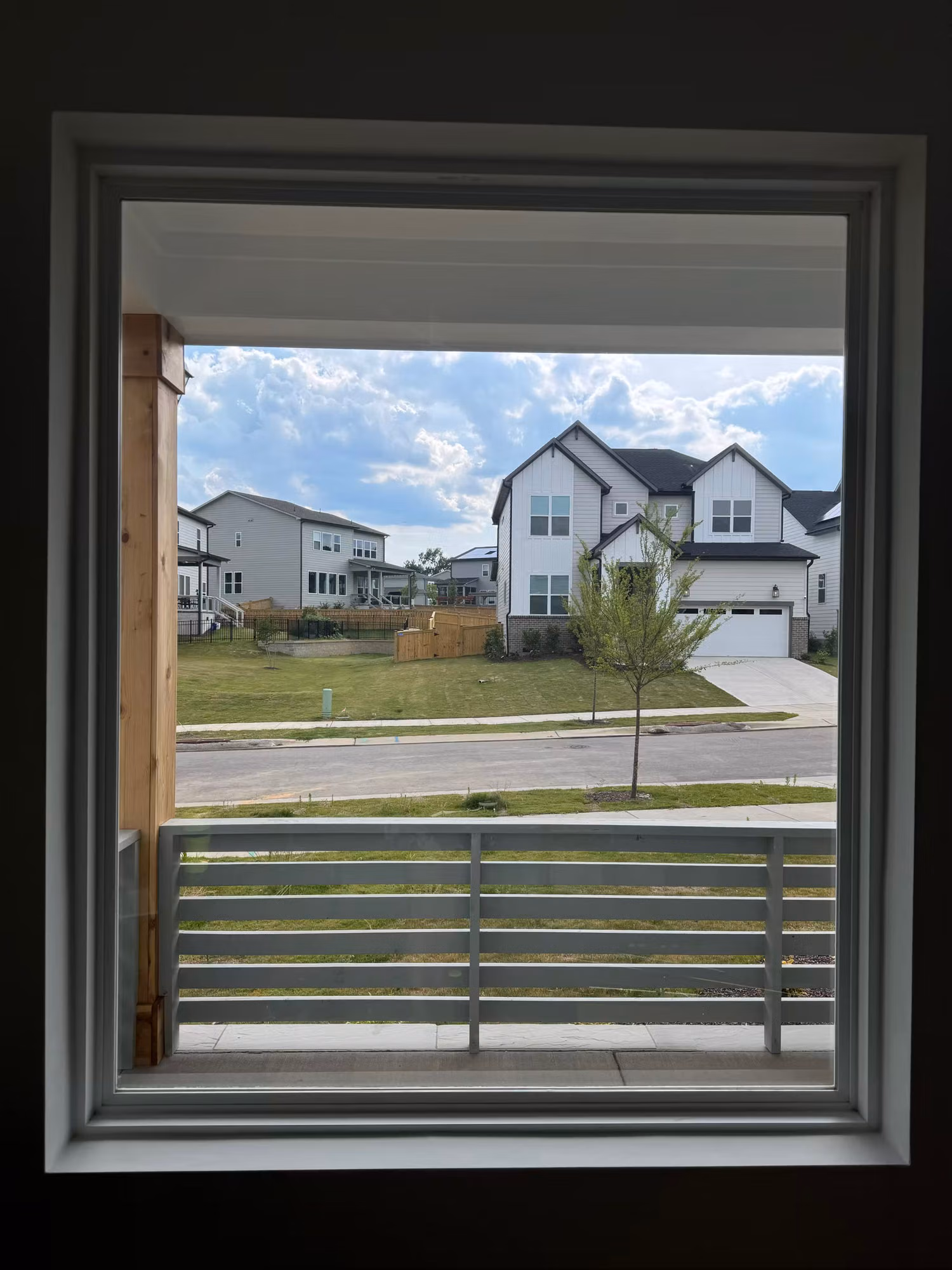 An upstairs picture window looking out over a residential street and houses across the way.