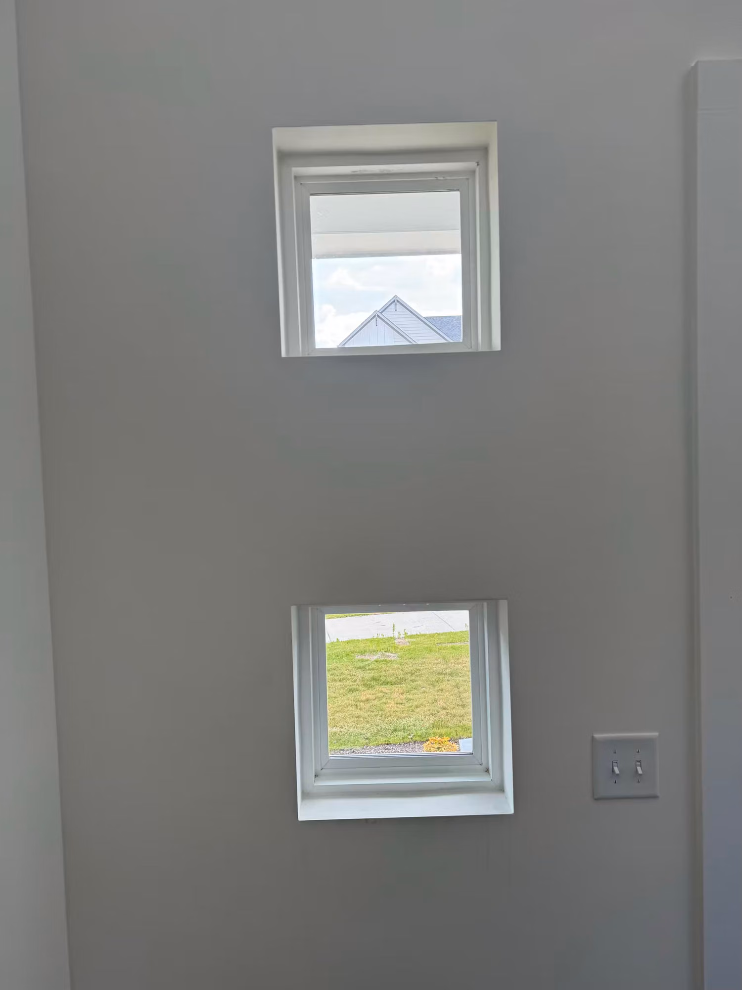 Two small stacked windows on a stairwell wall showing tinted glass with a rooftop and lawn view.