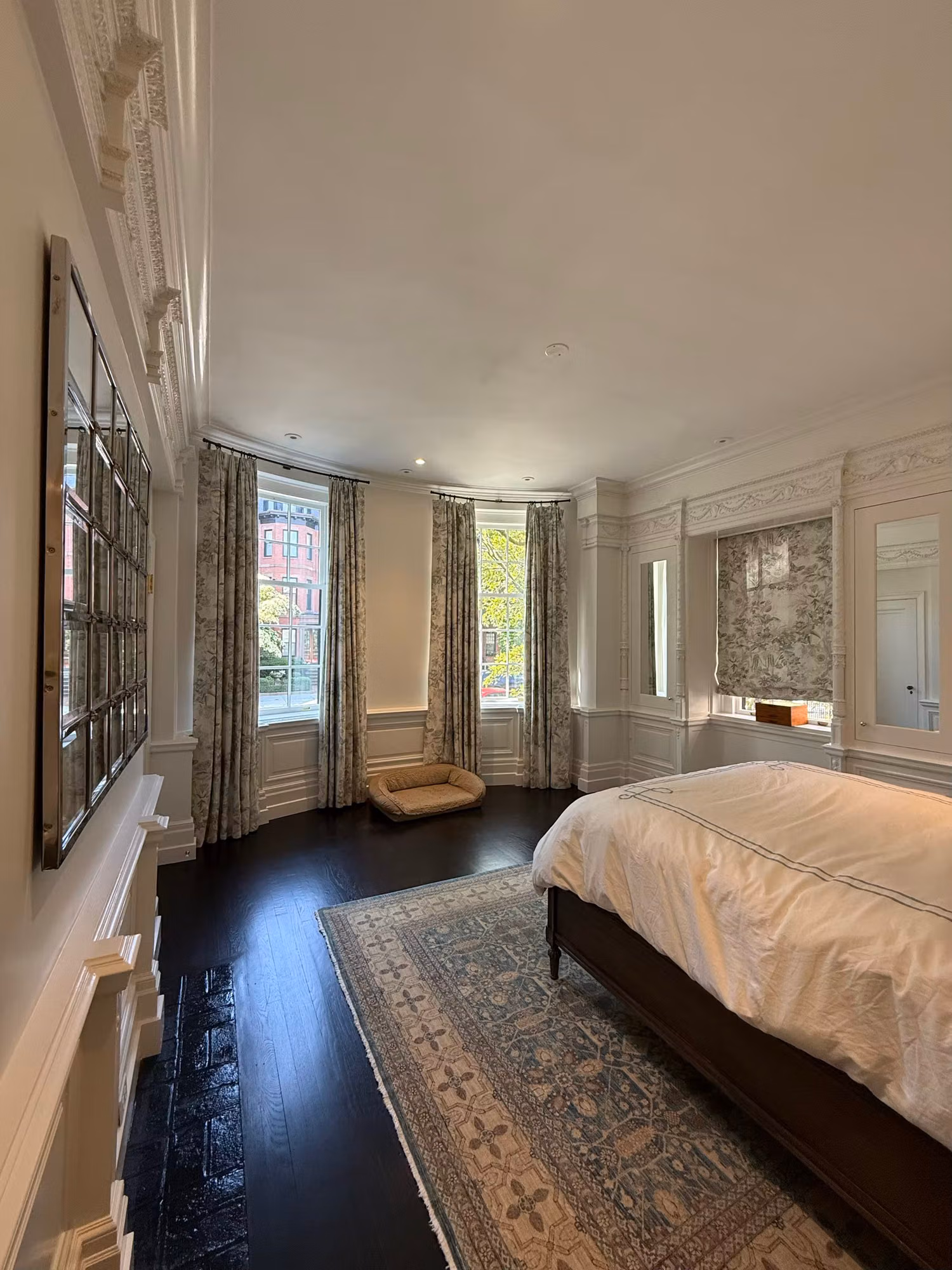 Wide view of a bedroom with a curved bay of clear divided-light windows, drapery, and framed wall art.