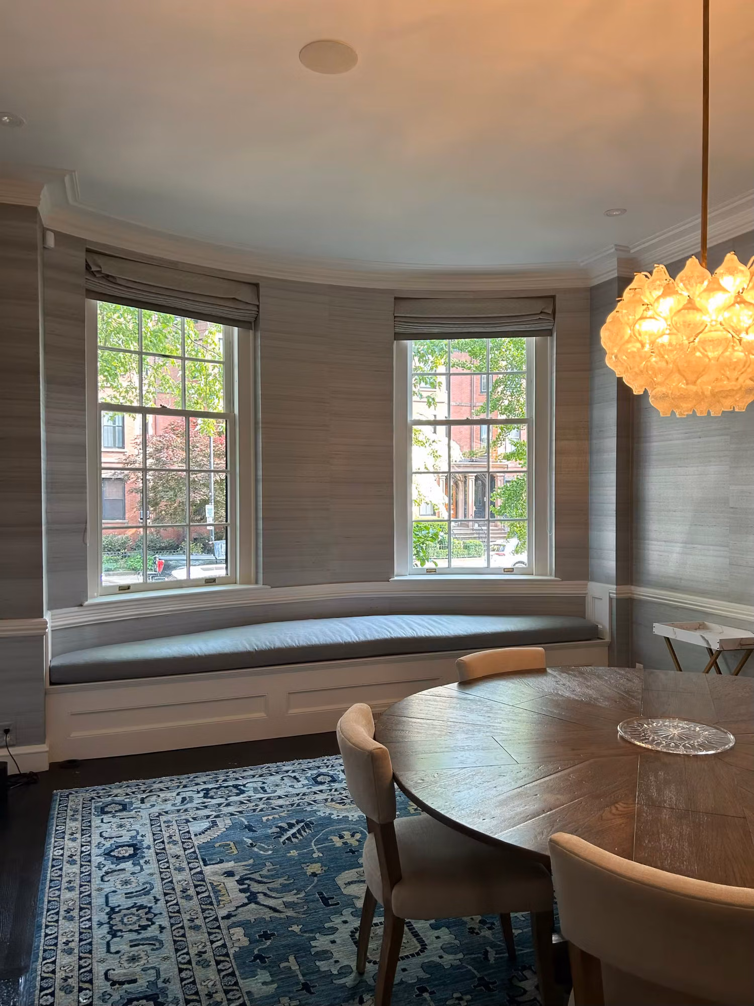 Curved bay window with grid panes and a built-in window seat in a dining area with a round table and patterned rug.