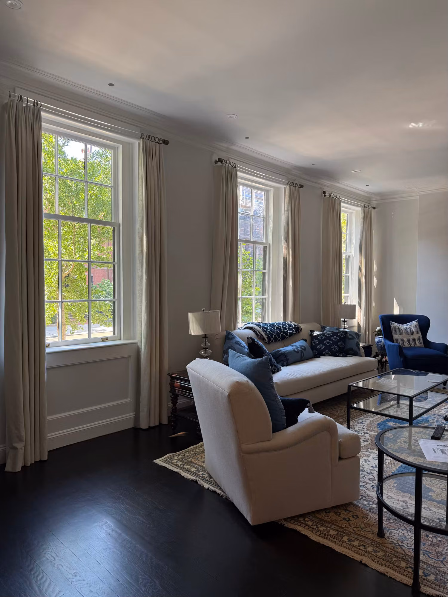 Tall divided-light double-hung living room windows with floor-length drapes flanking a seating area.
