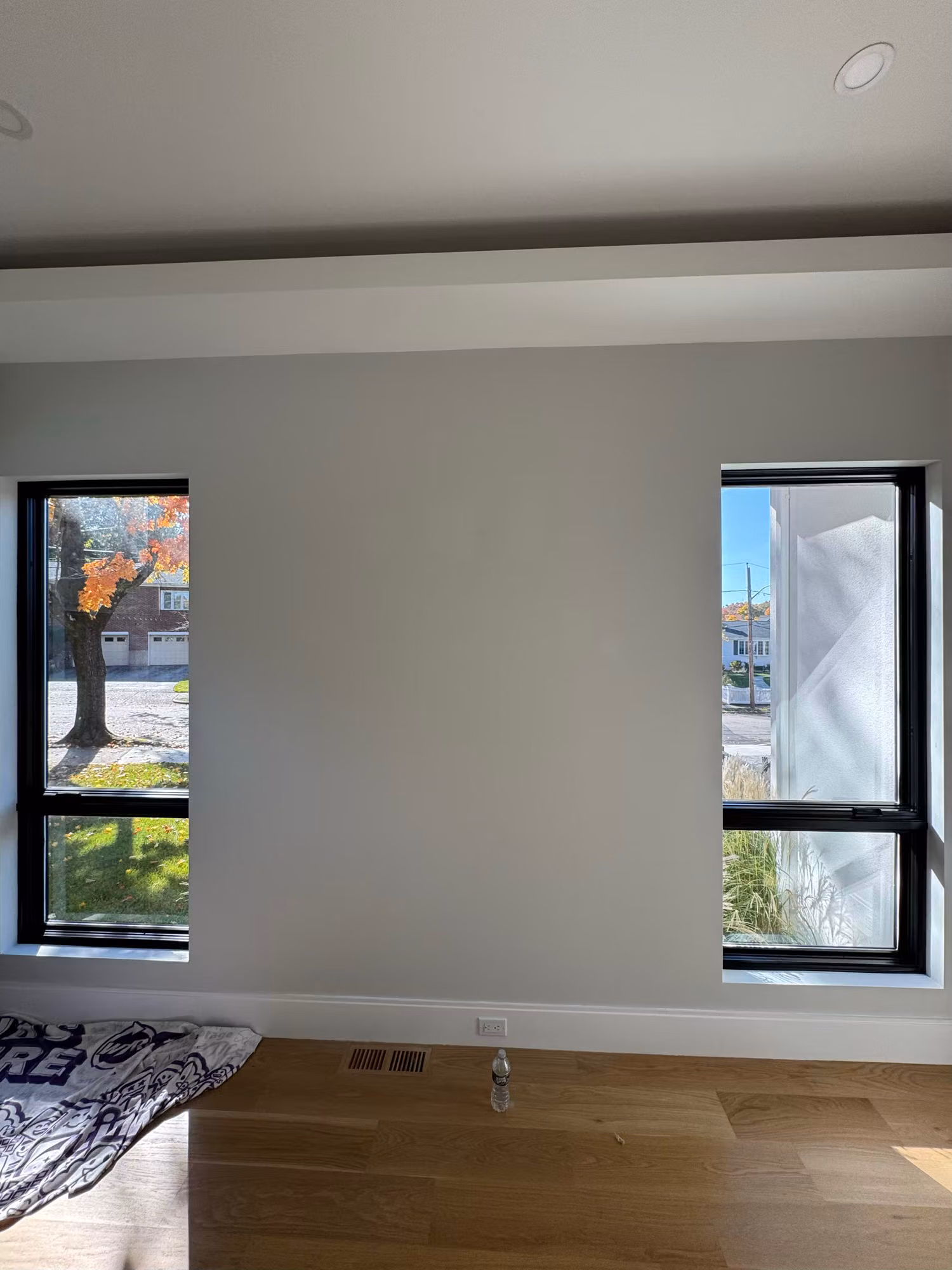 Two black-framed windows in a bright upper-floor bedroom overlooking rooftops and trees.