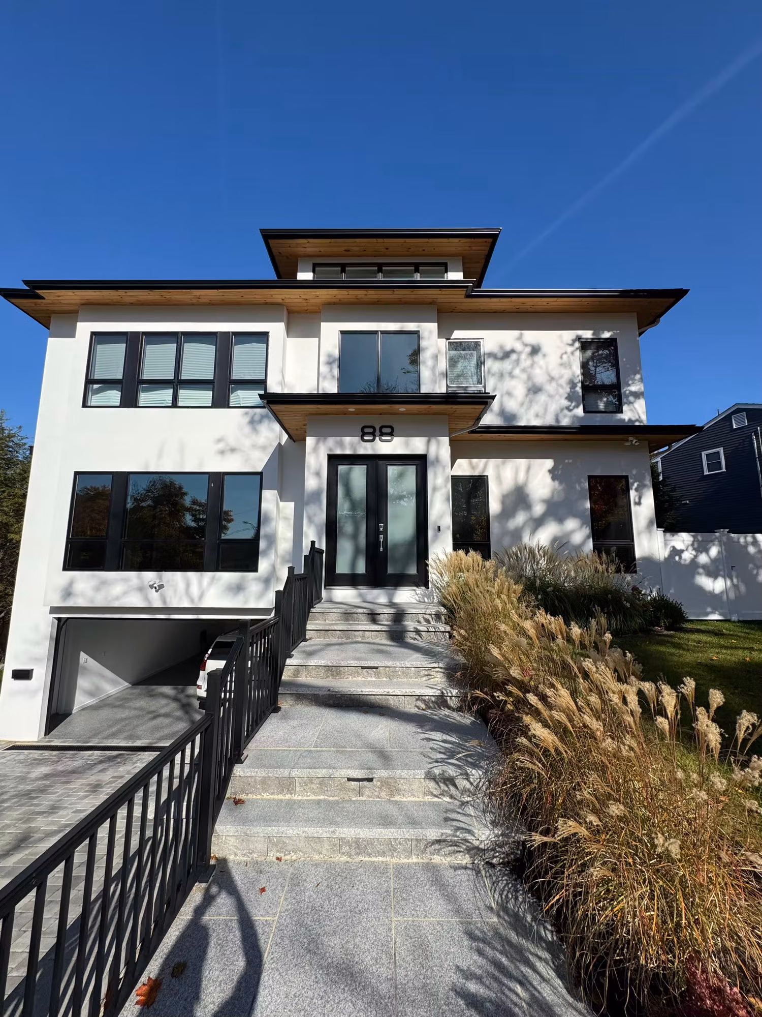 Modern two-story home exterior with many black-framed windows along a landscaped front entry.