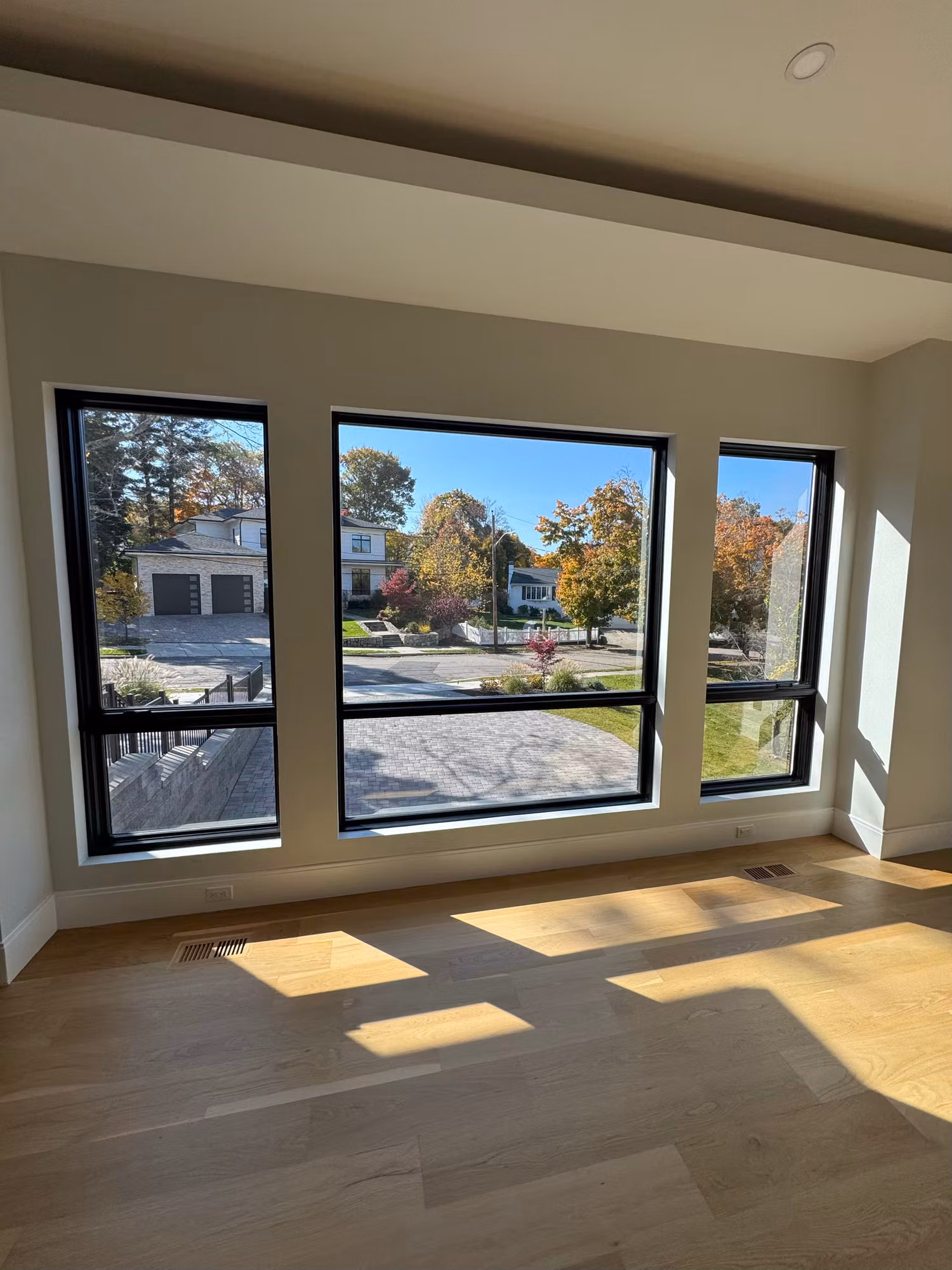 Three black-framed living room picture windows overlooking a residential street after film service.