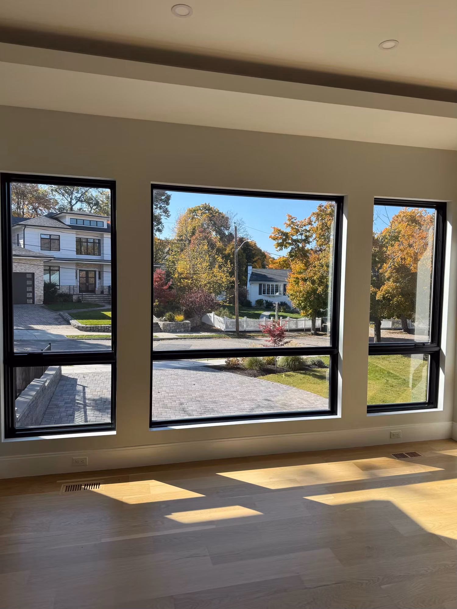 Three black-framed picture windows in an empty living room overlooking neighboring homes.