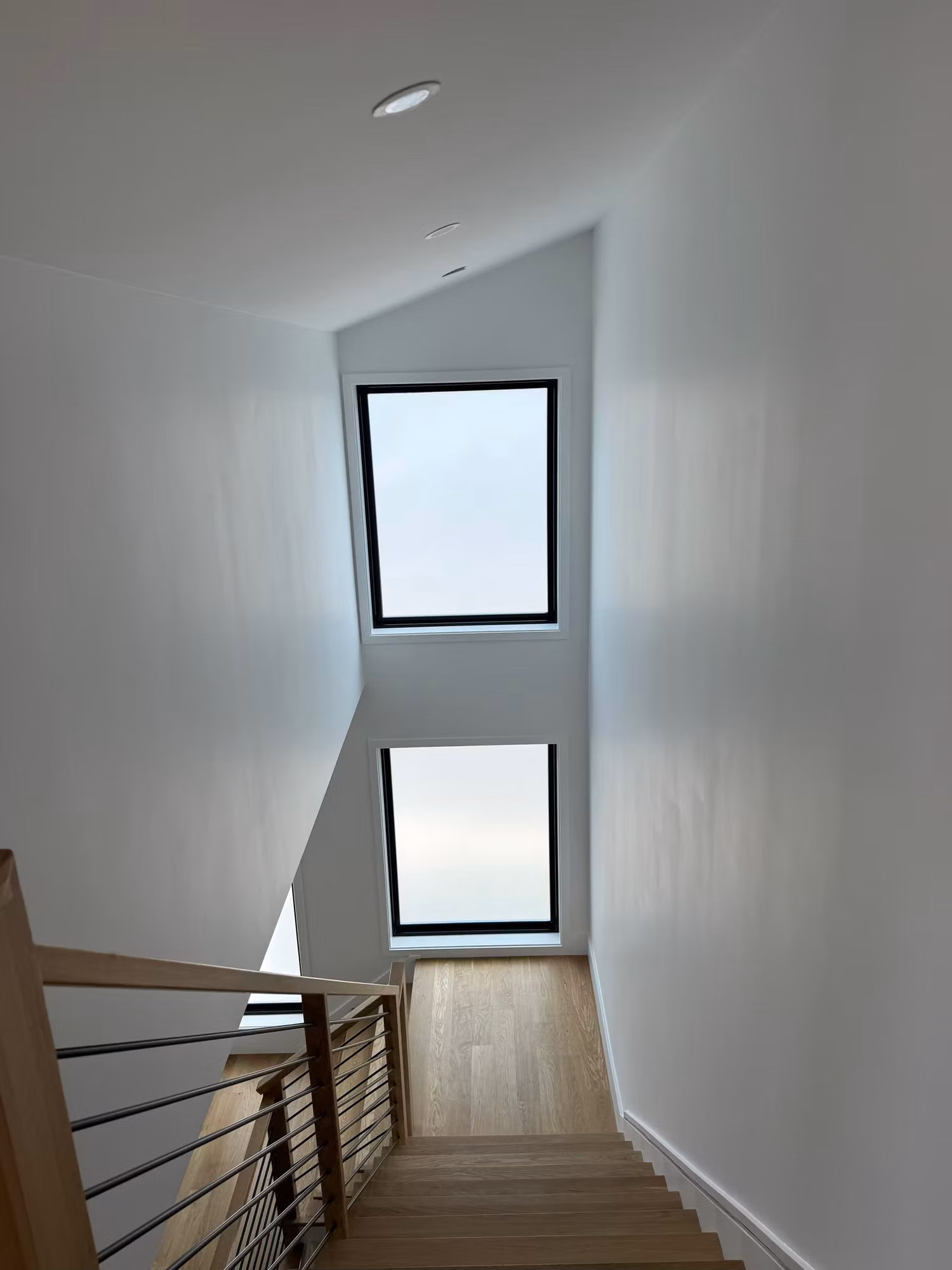 Two stacked tall stairwell windows treated with white frosted privacy film above a wood staircase.