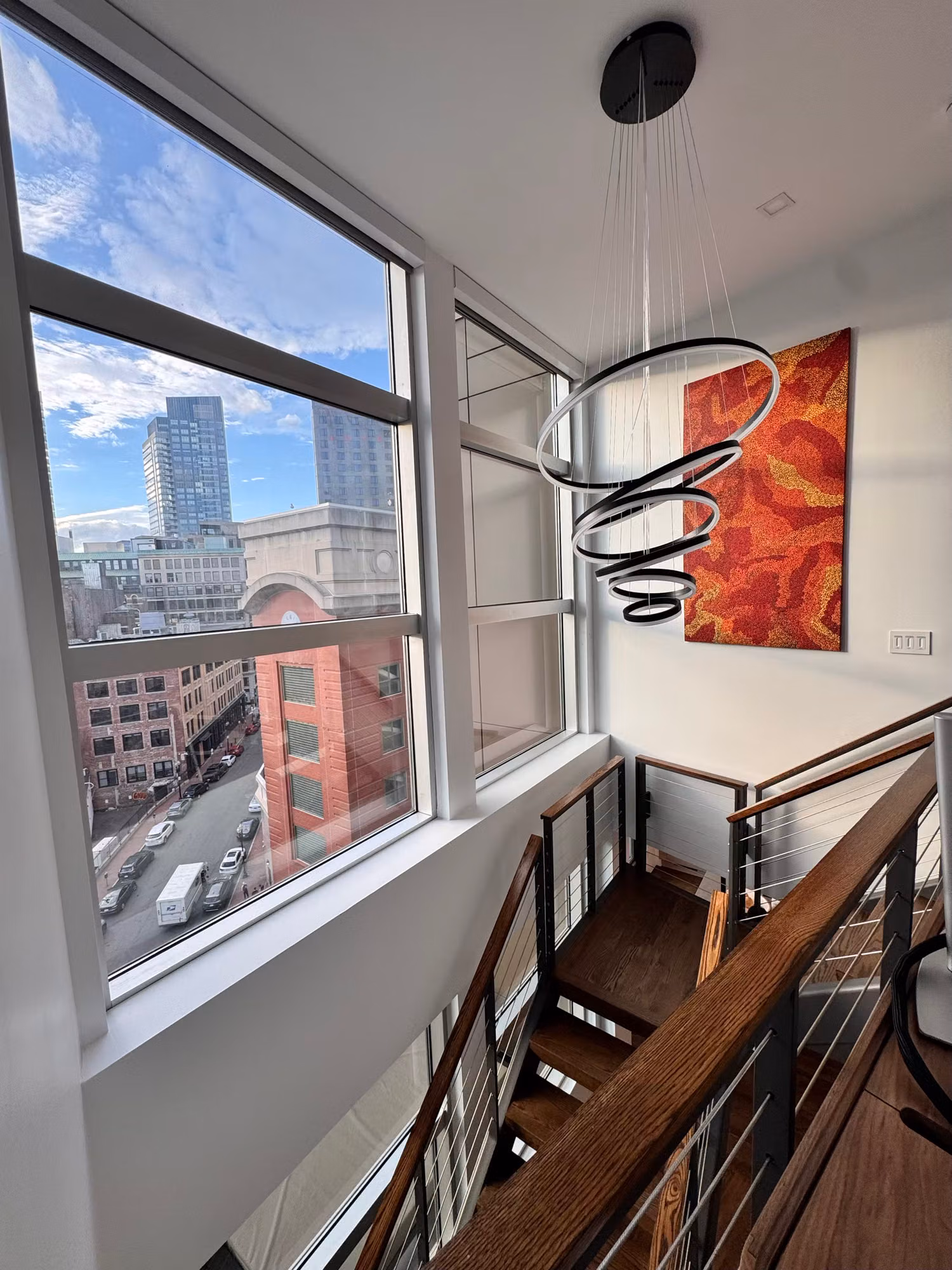 Tall penthouse stairwell windows with filmed glass beside a staircase, looking out over the city below.