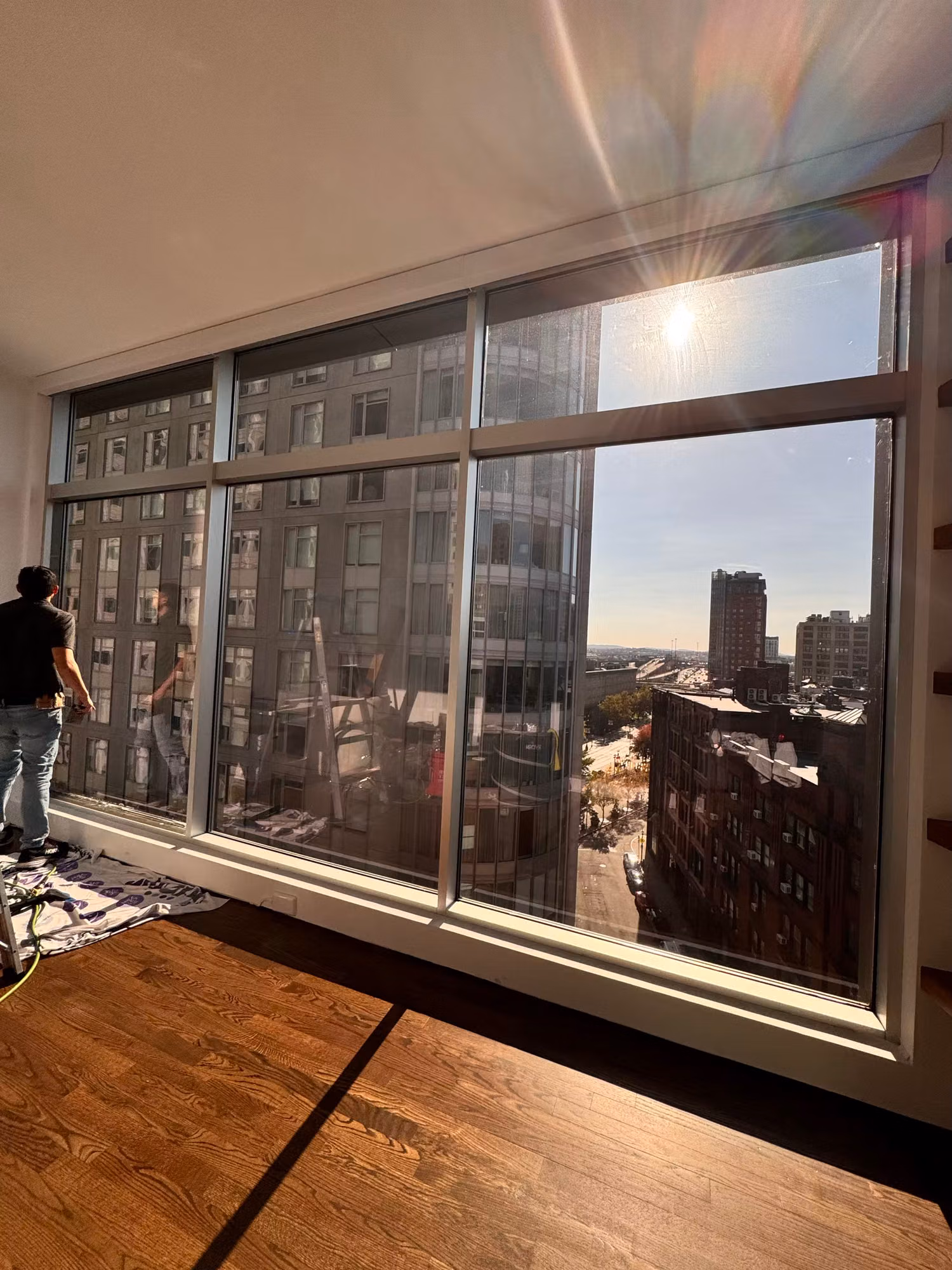 Installer fitting solar control film to a wall of floor-to-ceiling high-rise windows overlooking the city.