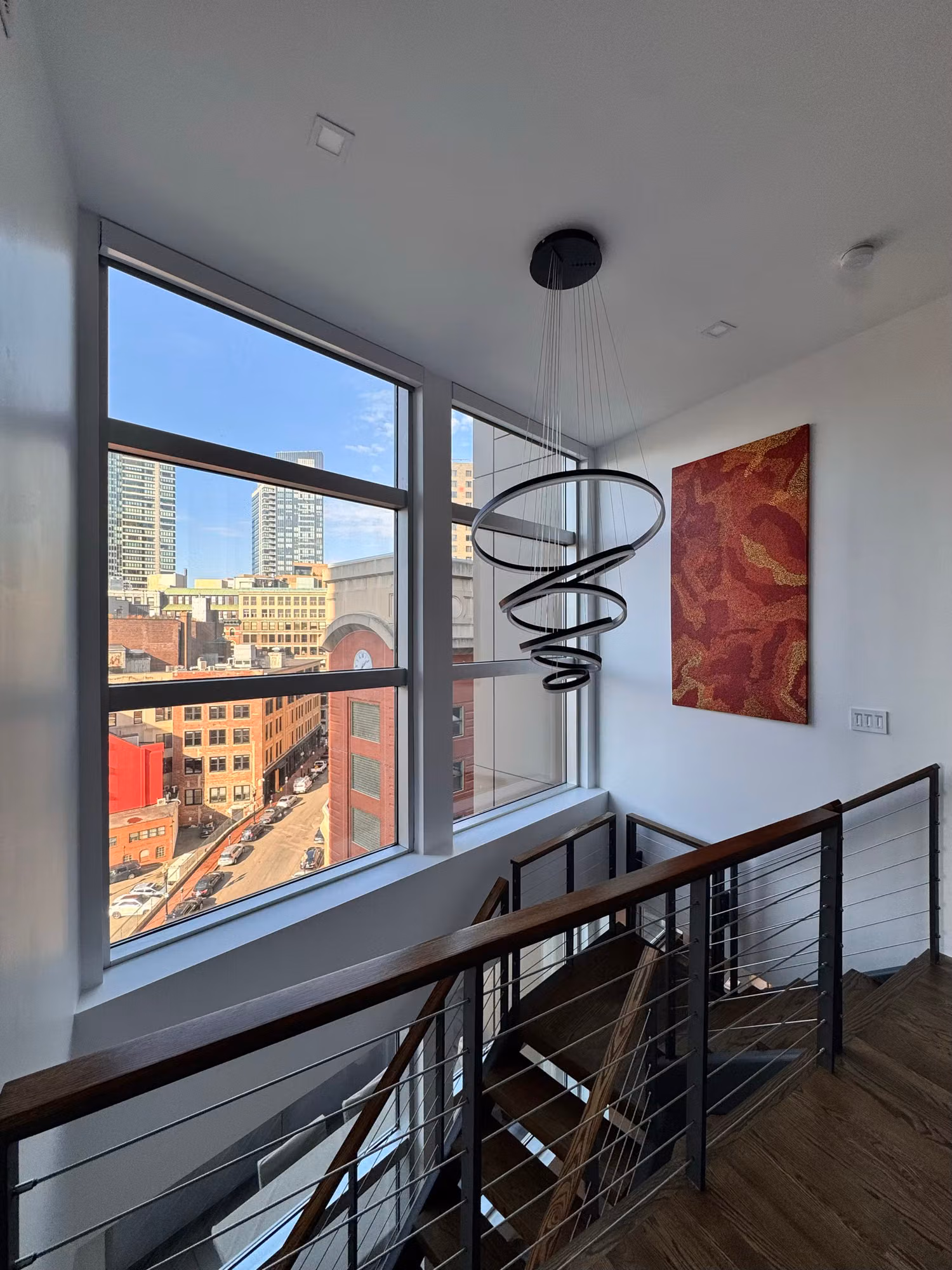 Stairwell landing window over a glass-railing staircase with solar control film softening the city view light.