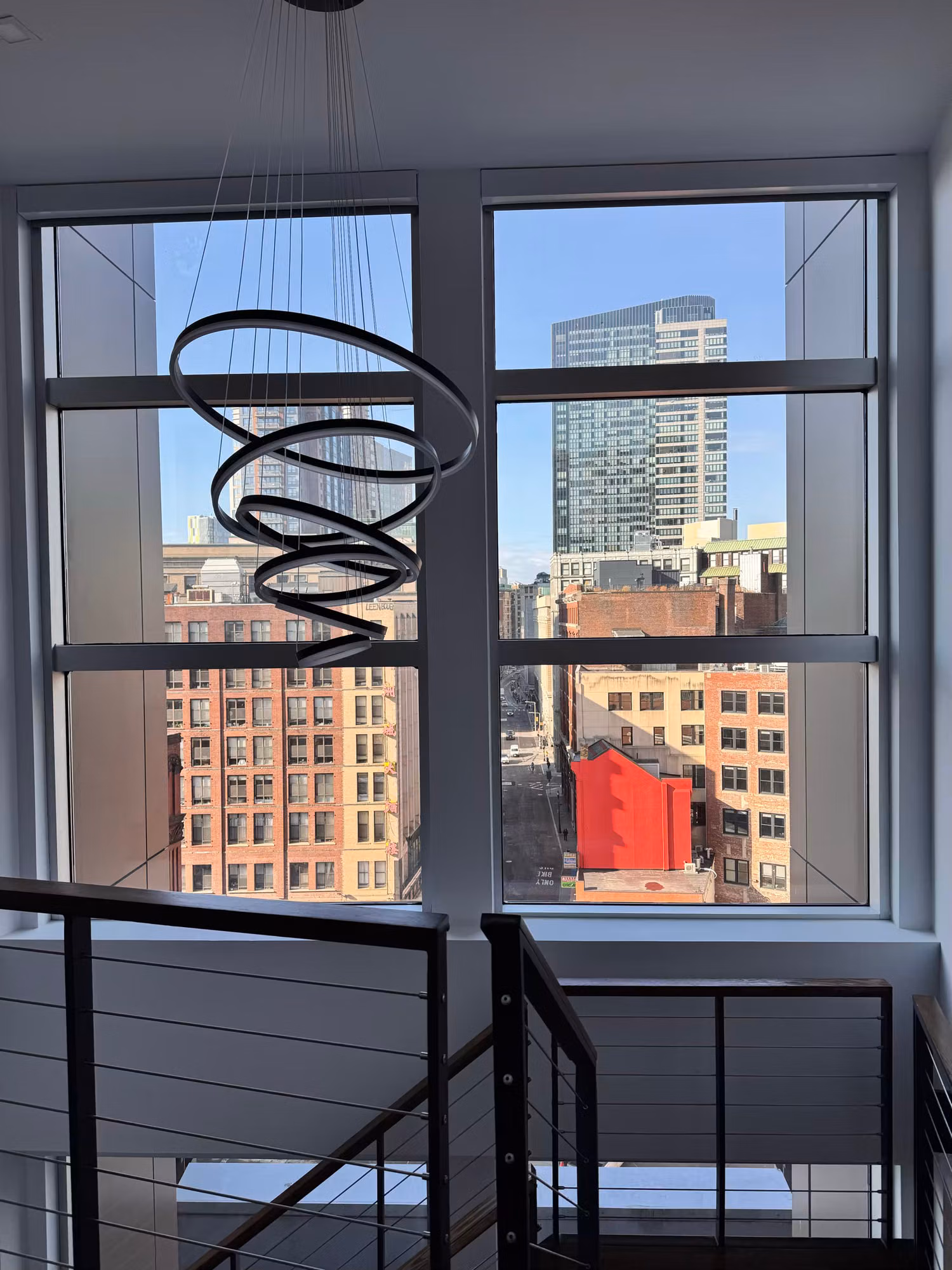 Tall stairwell windows above a glass-railing staircase with solar control film tempering the bright skyline light.