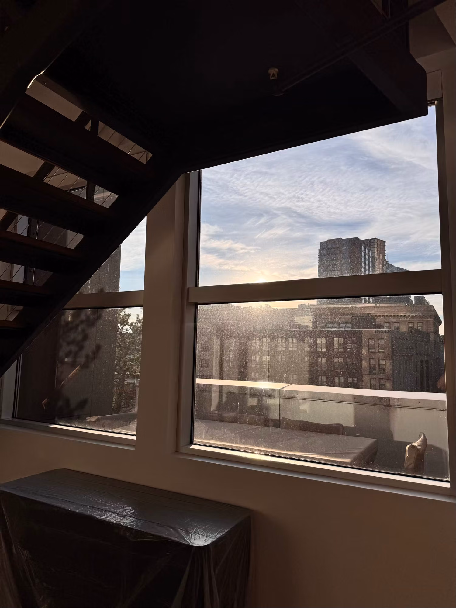 Stairwell window with solar control film cutting low-angle sun glare across a city rooftop view.