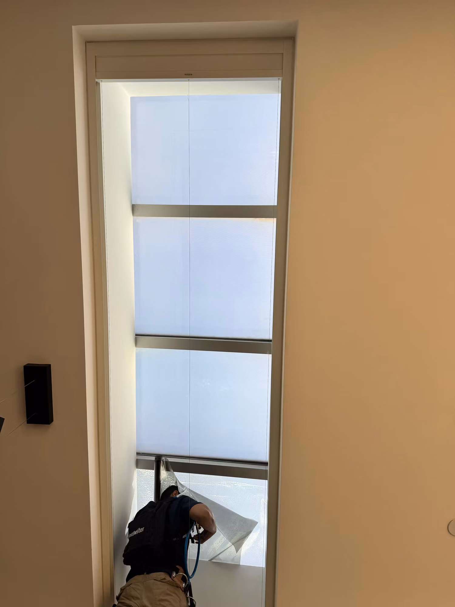 Tall narrow window fitted with frosted light-diffusing film while an installer works at the base of the glass.