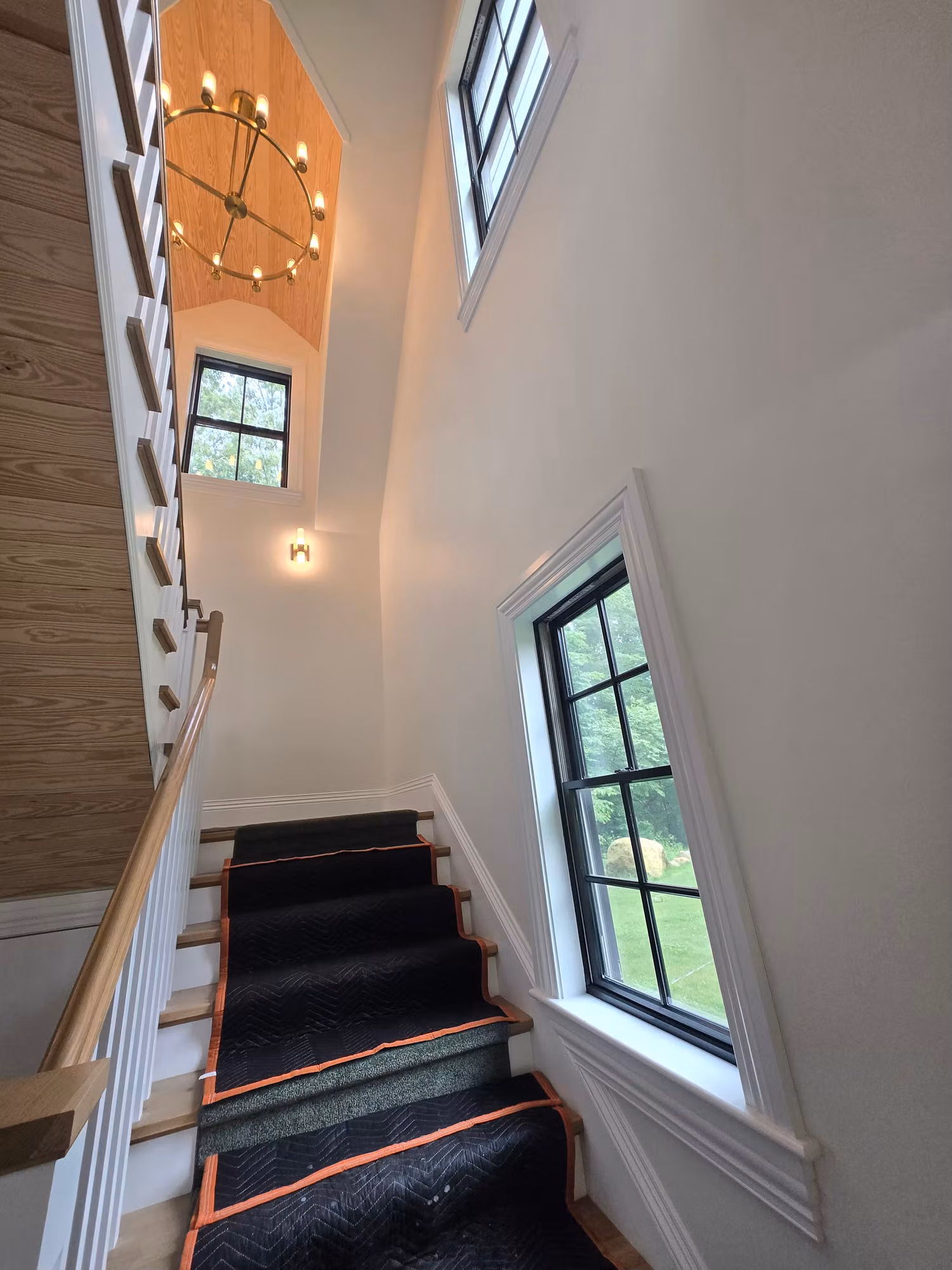 Interior staircase with a tall side window and arched transom window above, both glazed with clear safety film.
