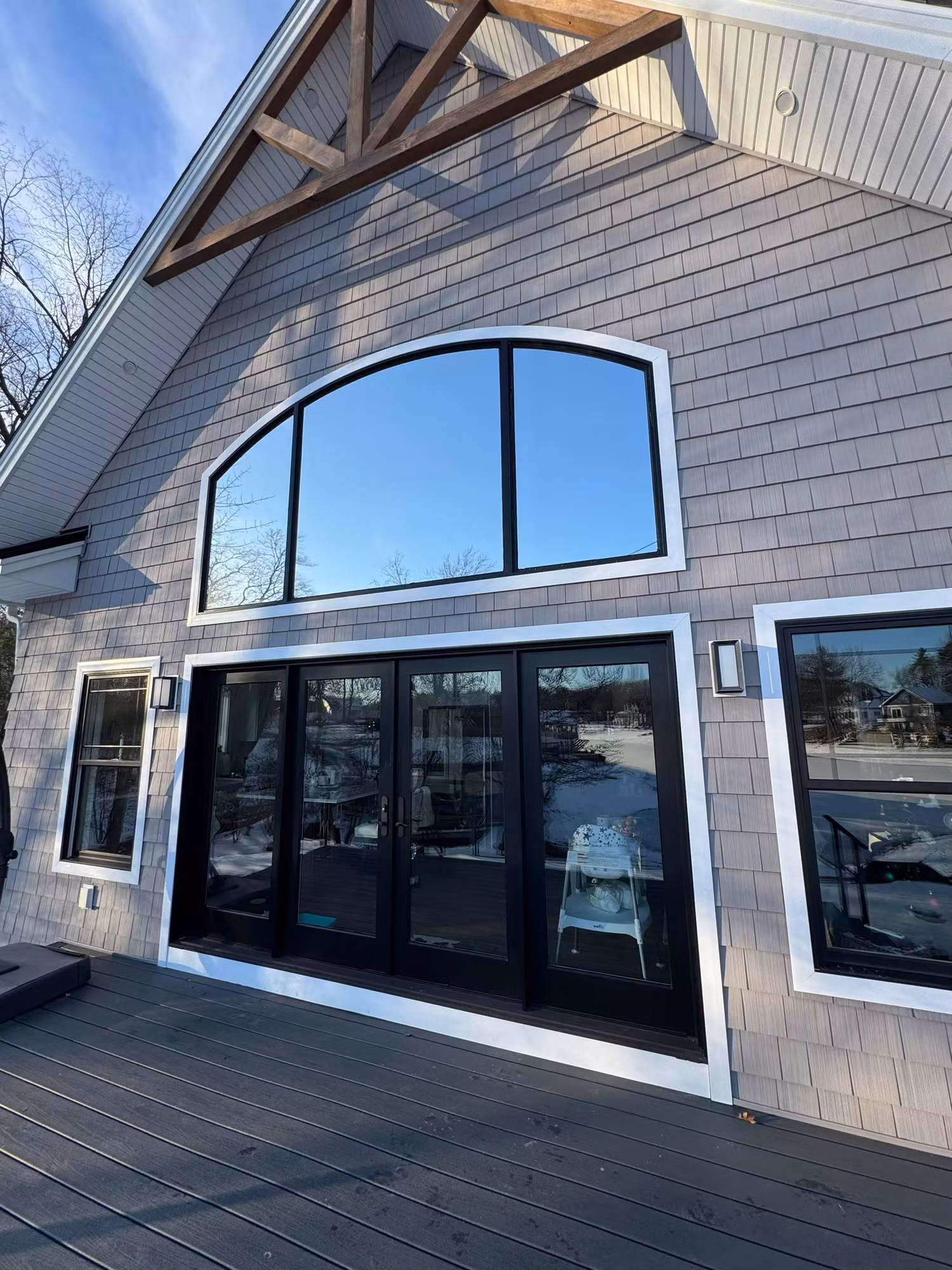 Mirror-finish silver solar film on the arched gable window and patio doors of a shingle-sided home.