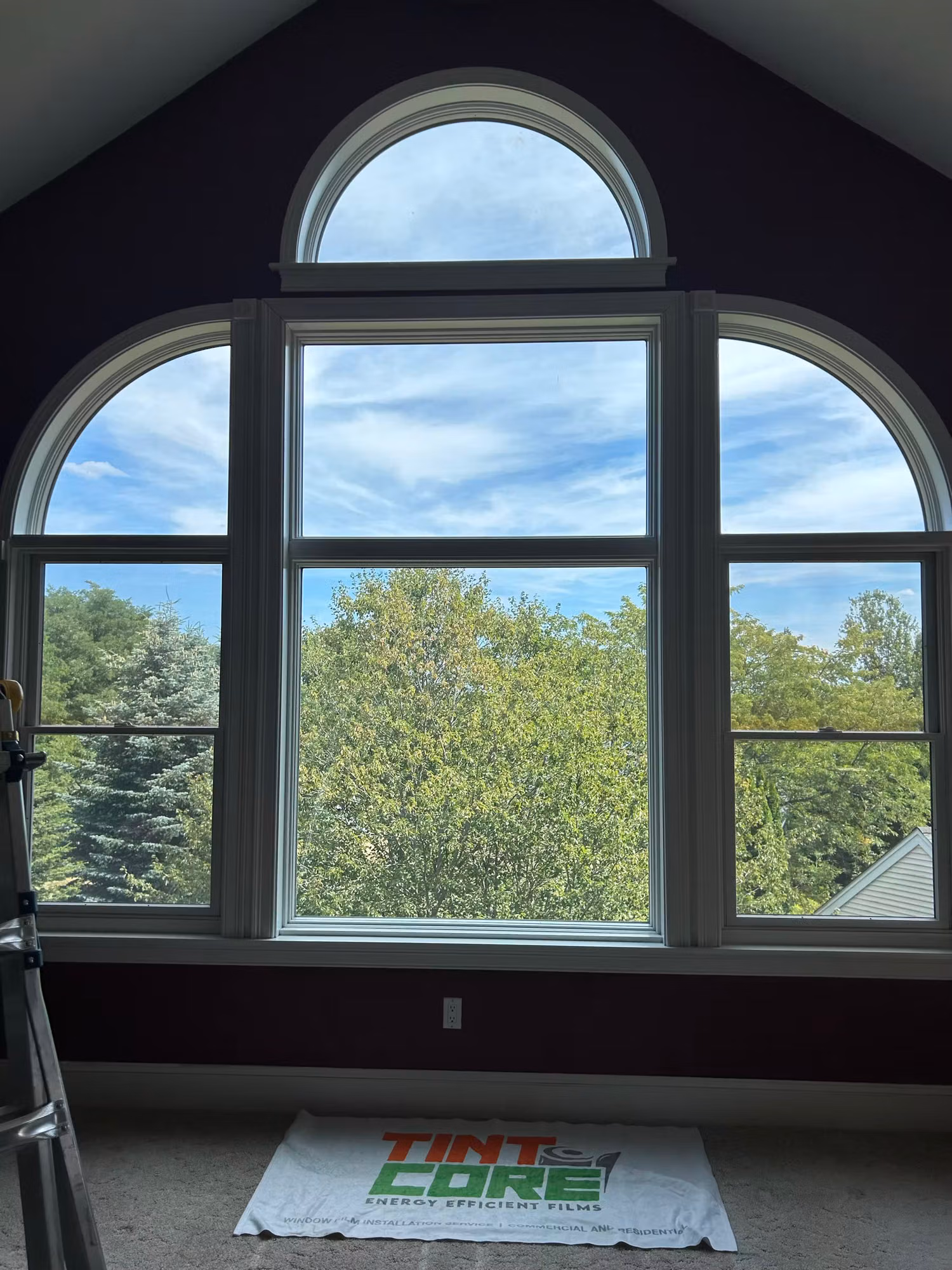 Arched palladian window unit in a vaulted bedroom during window film installation with a protective drop cloth.