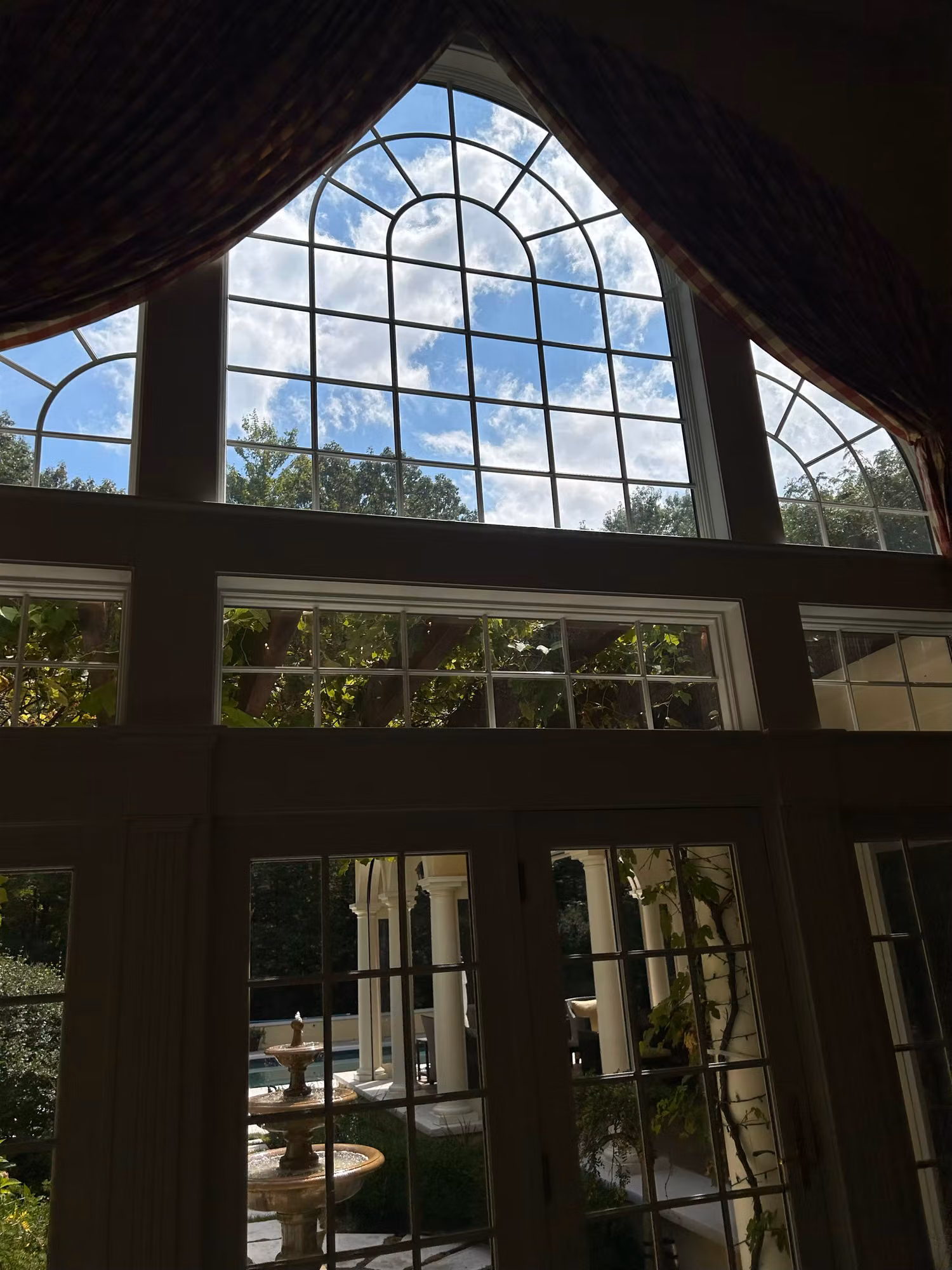 Interior view of an arched palladian fan window above French doors overlooking a courtyard fountain.