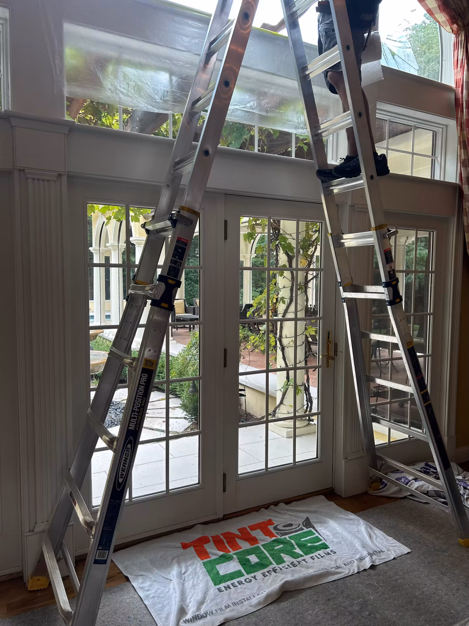 Ladders set up against French doors and sidelights during a residential window film installation.
