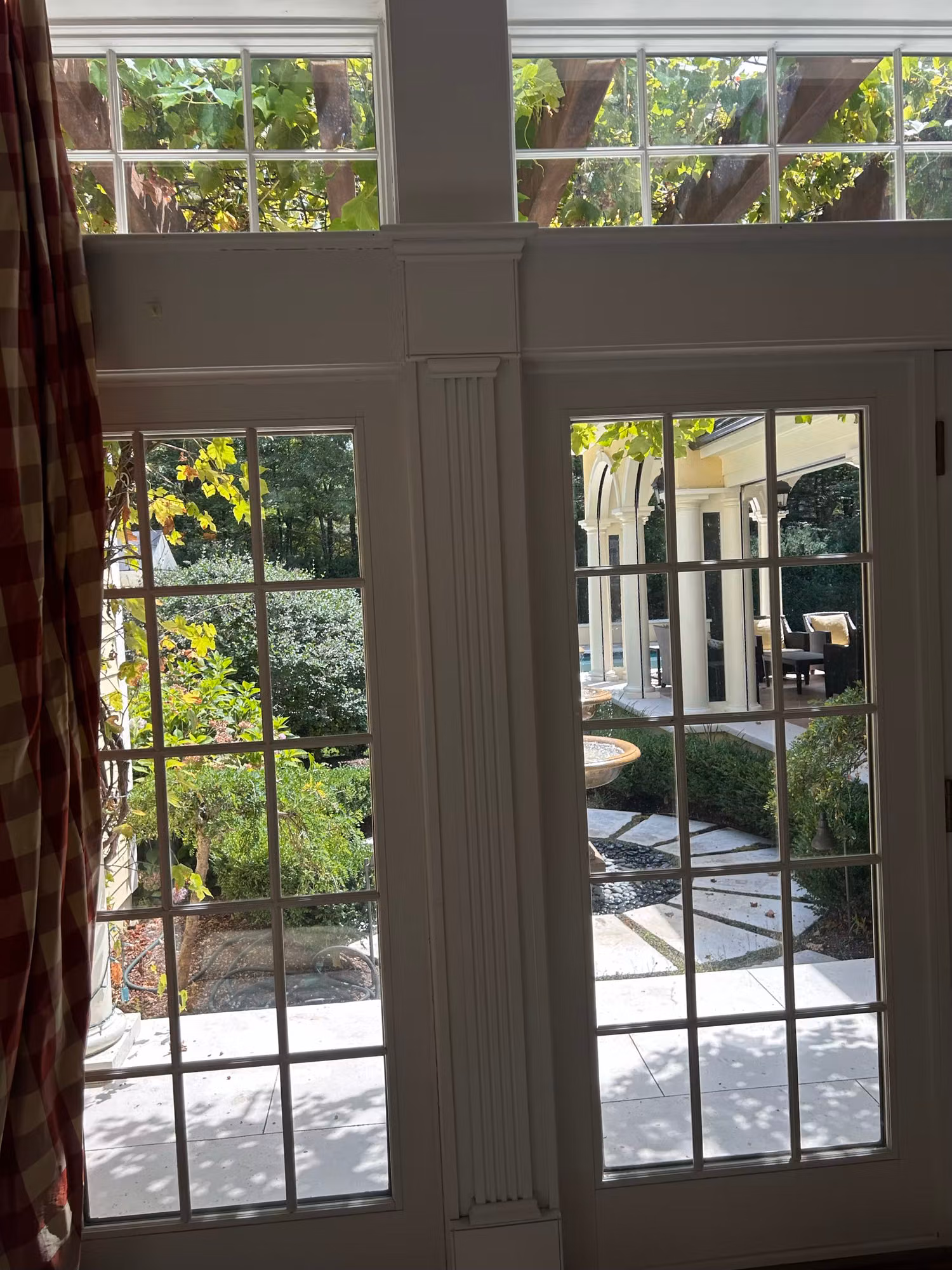 Divided-lite French doors and transom windows with clear film looking out onto a garden patio.