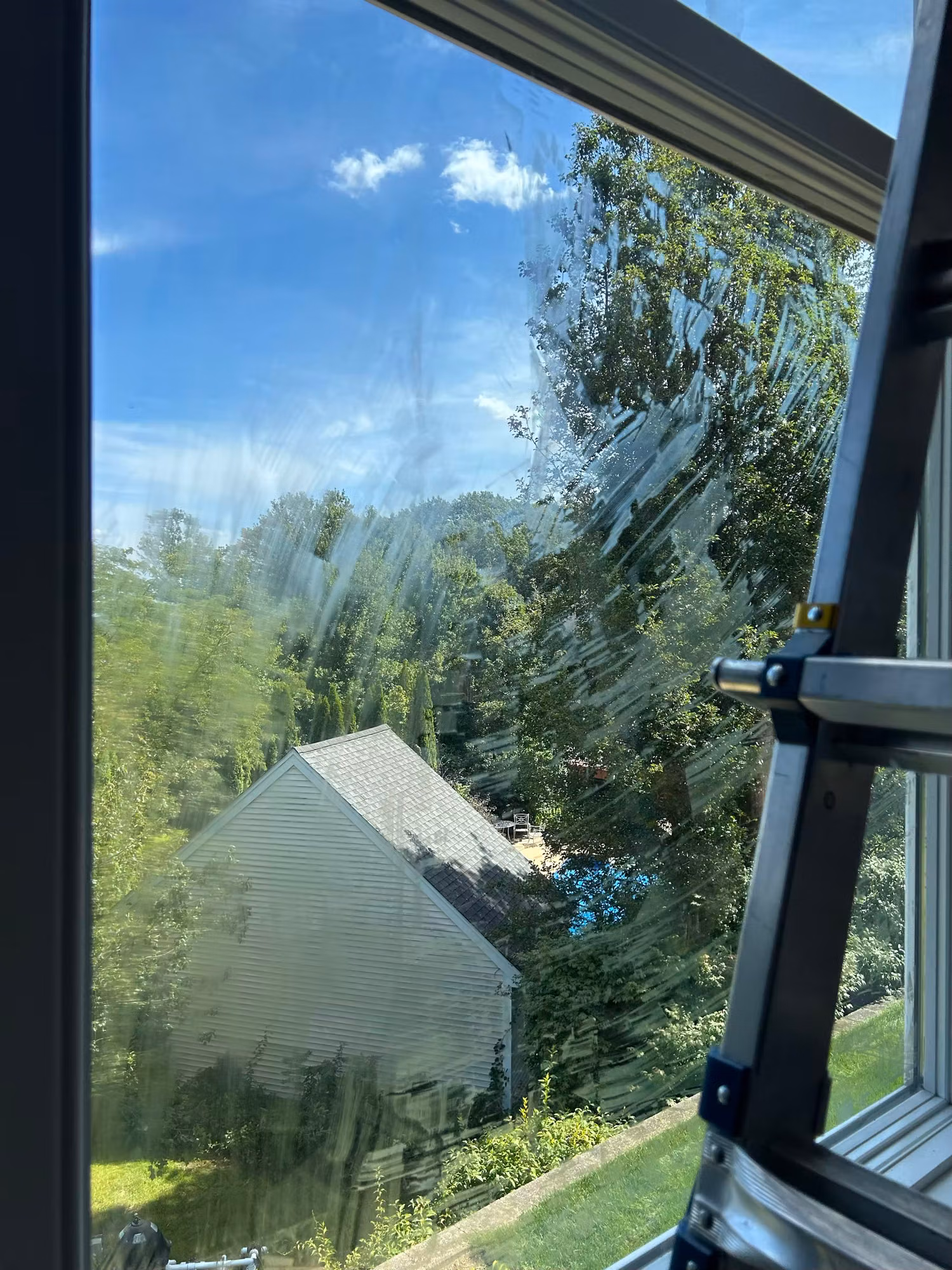 Freshly applied window film on an upper-floor home window overlooking a neighboring house and trees, with squeegee marks still visible.