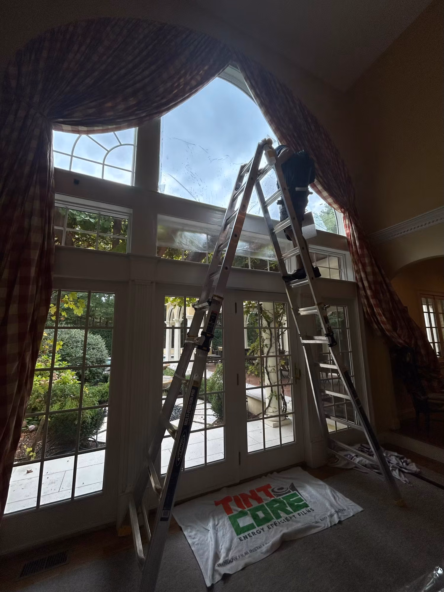 Tall arched French doors with sidelights and a transom during window film installation with a ladder in place.