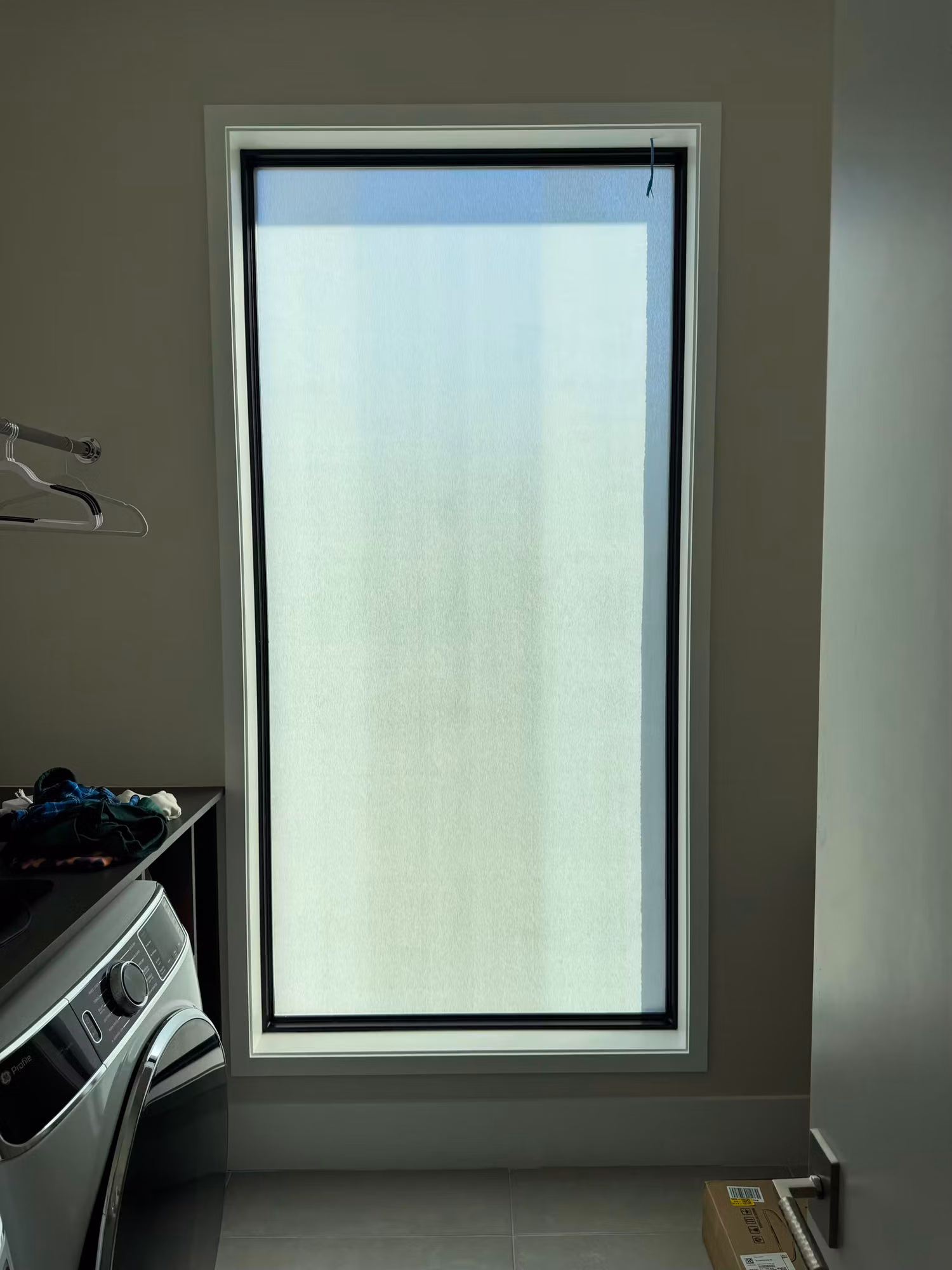 Tall laundry room window covered with translucent frosted privacy film that diffuses light while blocking the view.