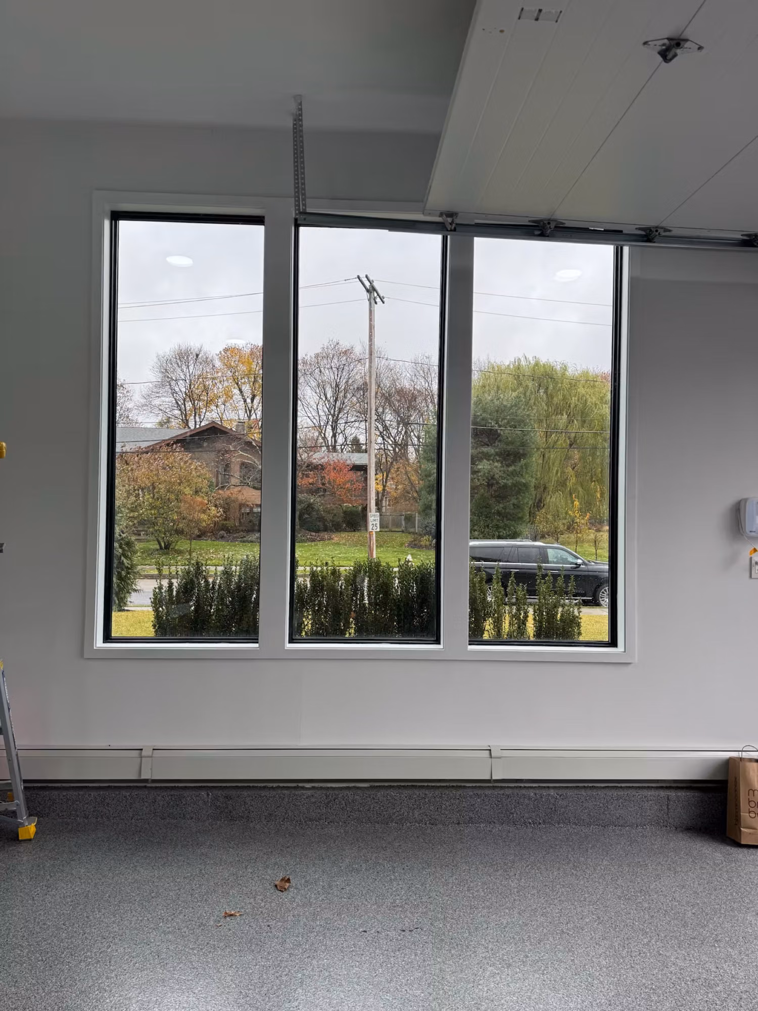 Three tall black-framed windows with clear glass before film, overlooking a yard and street.