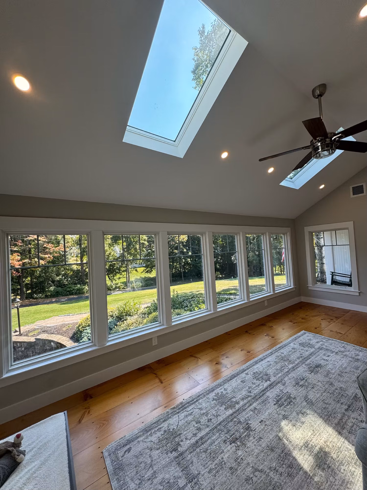 Vaulted sunroom with a long bank of windows and two skylights overlooking a green backyard.