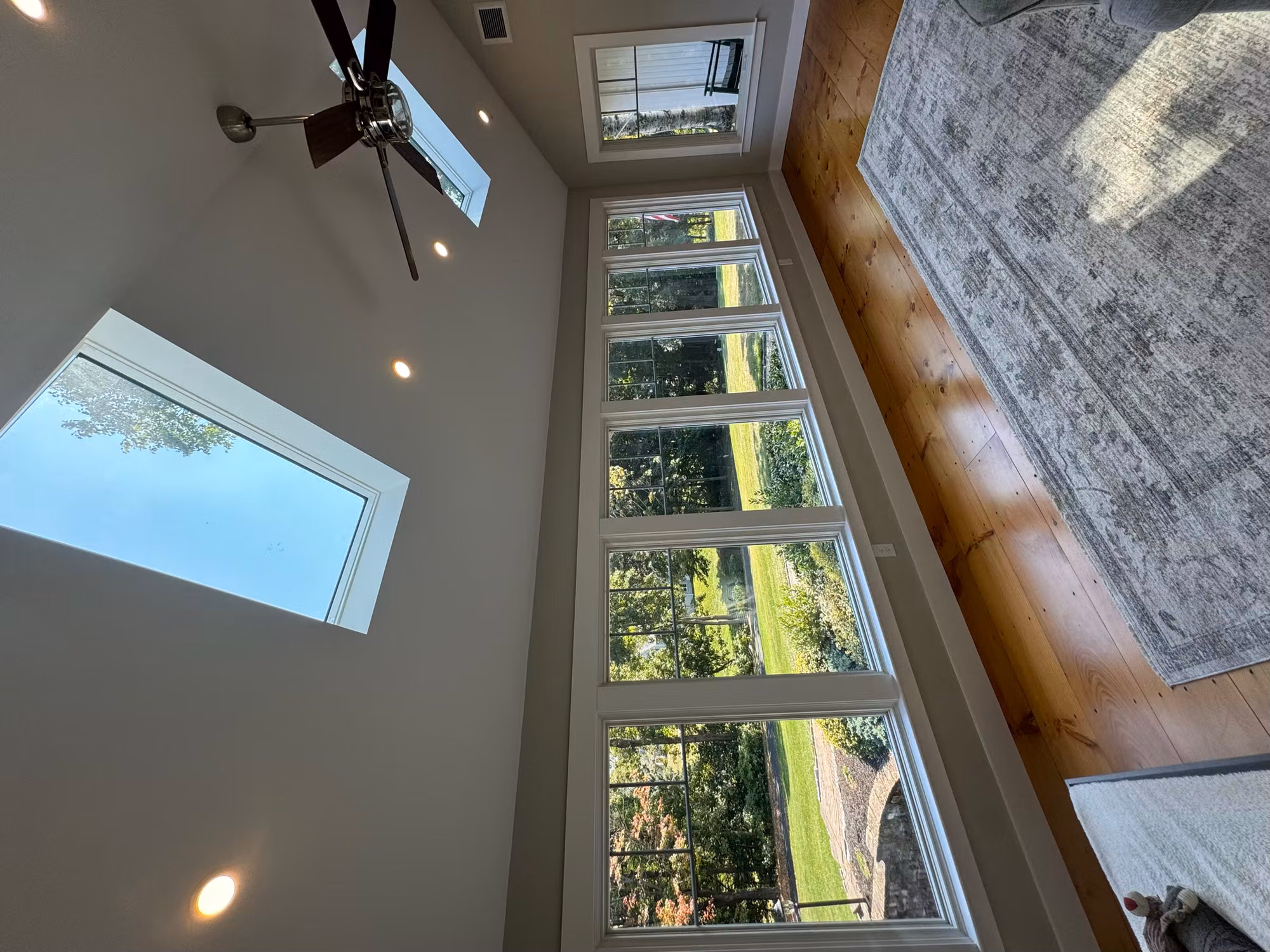 Bright vaulted sunroom showing a row of large windows and two skylights above hardwood floors.