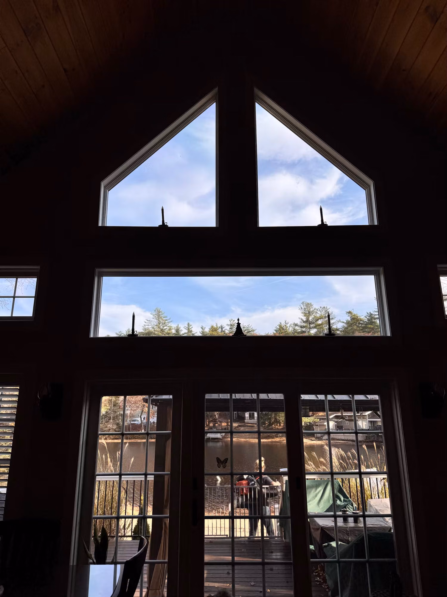 Triangular peak windows above a transom and French patio doors with sidelights, looking out to a bright sky and trees.