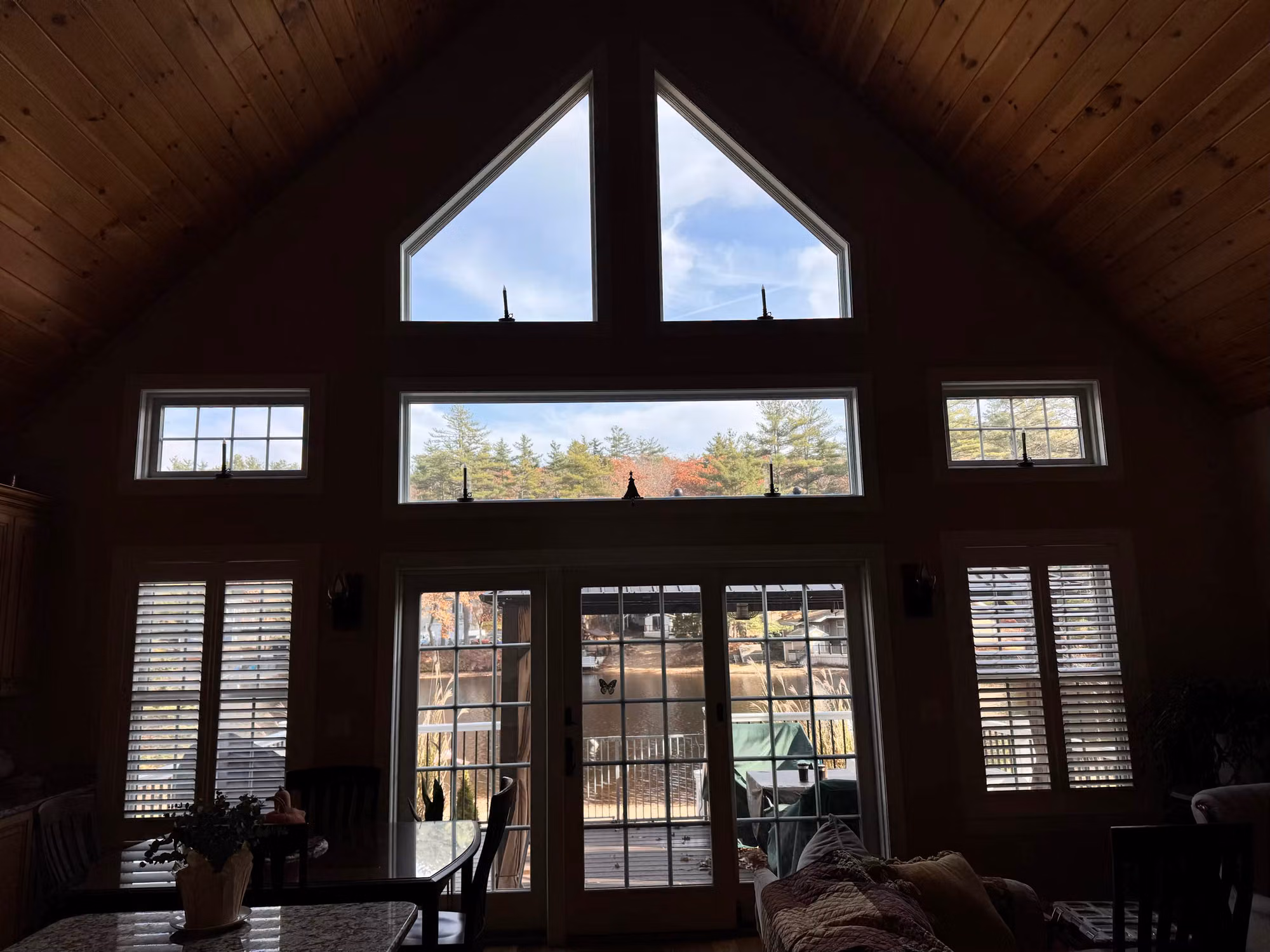 Great room window wall with triangular peak glass, transoms, and French patio doors with sidelights overlooking a wooded yard.