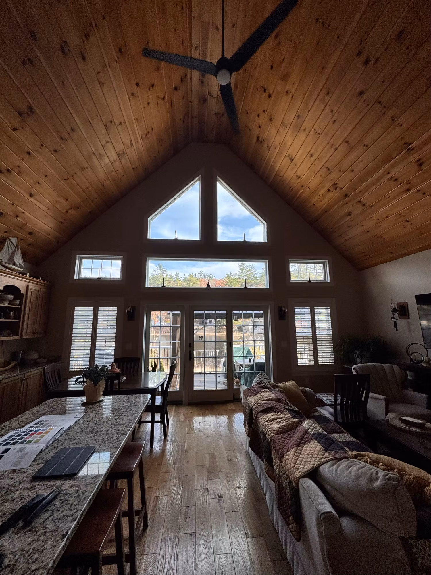 Vaulted living room with hardwood floors facing a tall window wall of peak glass, transoms, and French doors to a deck.