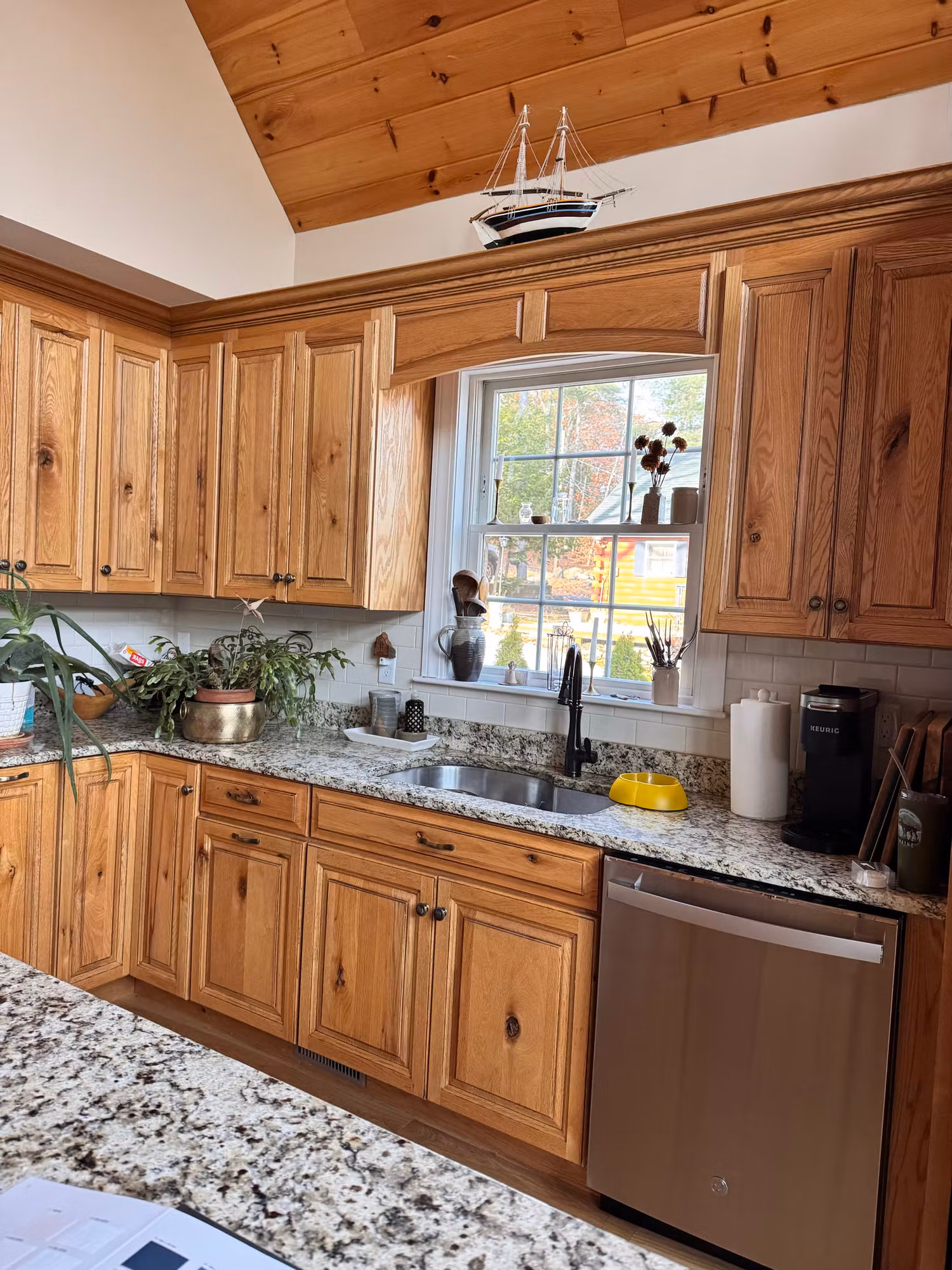 Kitchen sink window framed by wood cabinets and granite counter with film over the glass.