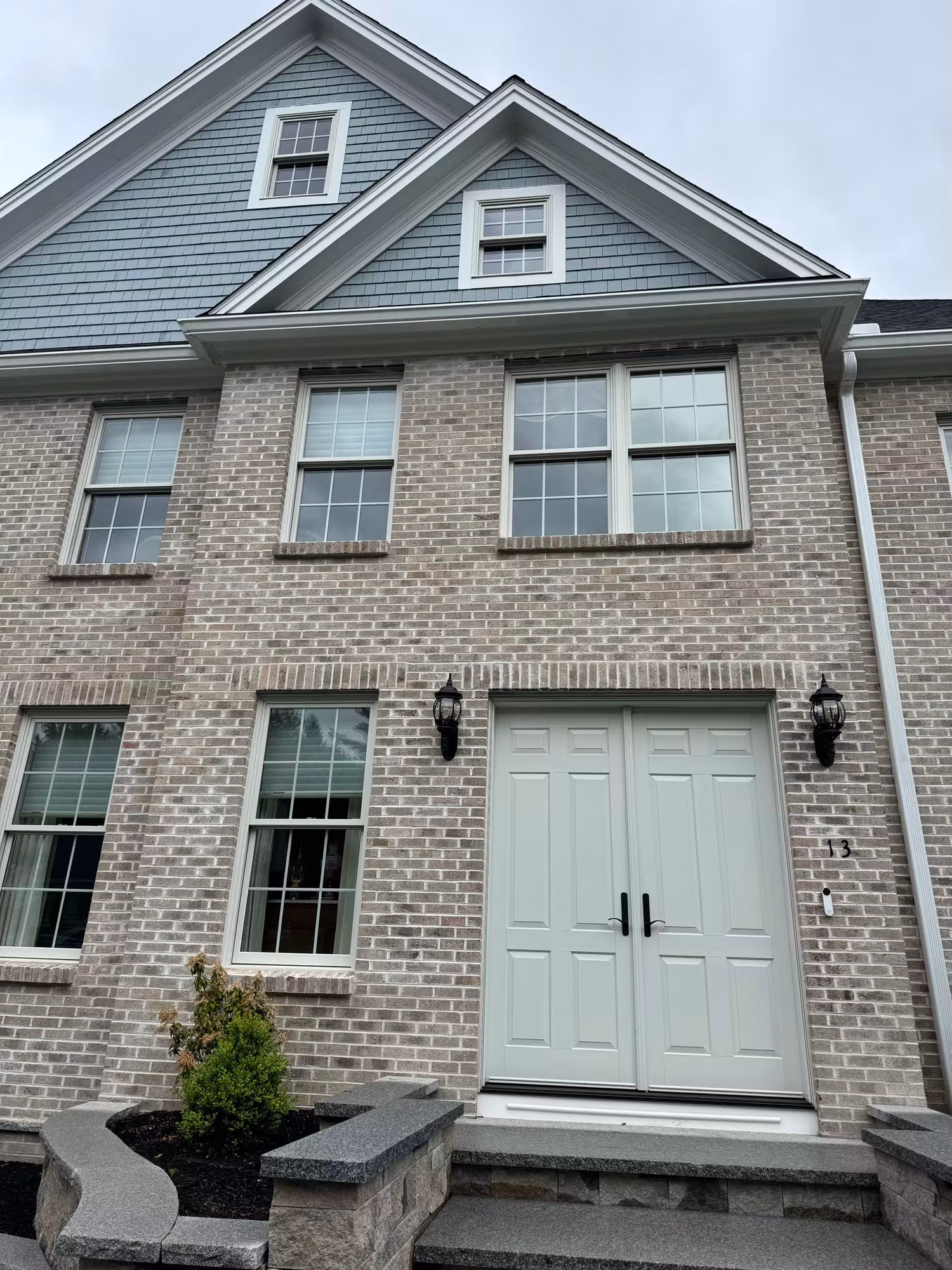 Front exterior of a brick townhome with double-hung windows and a light green double entry door.
