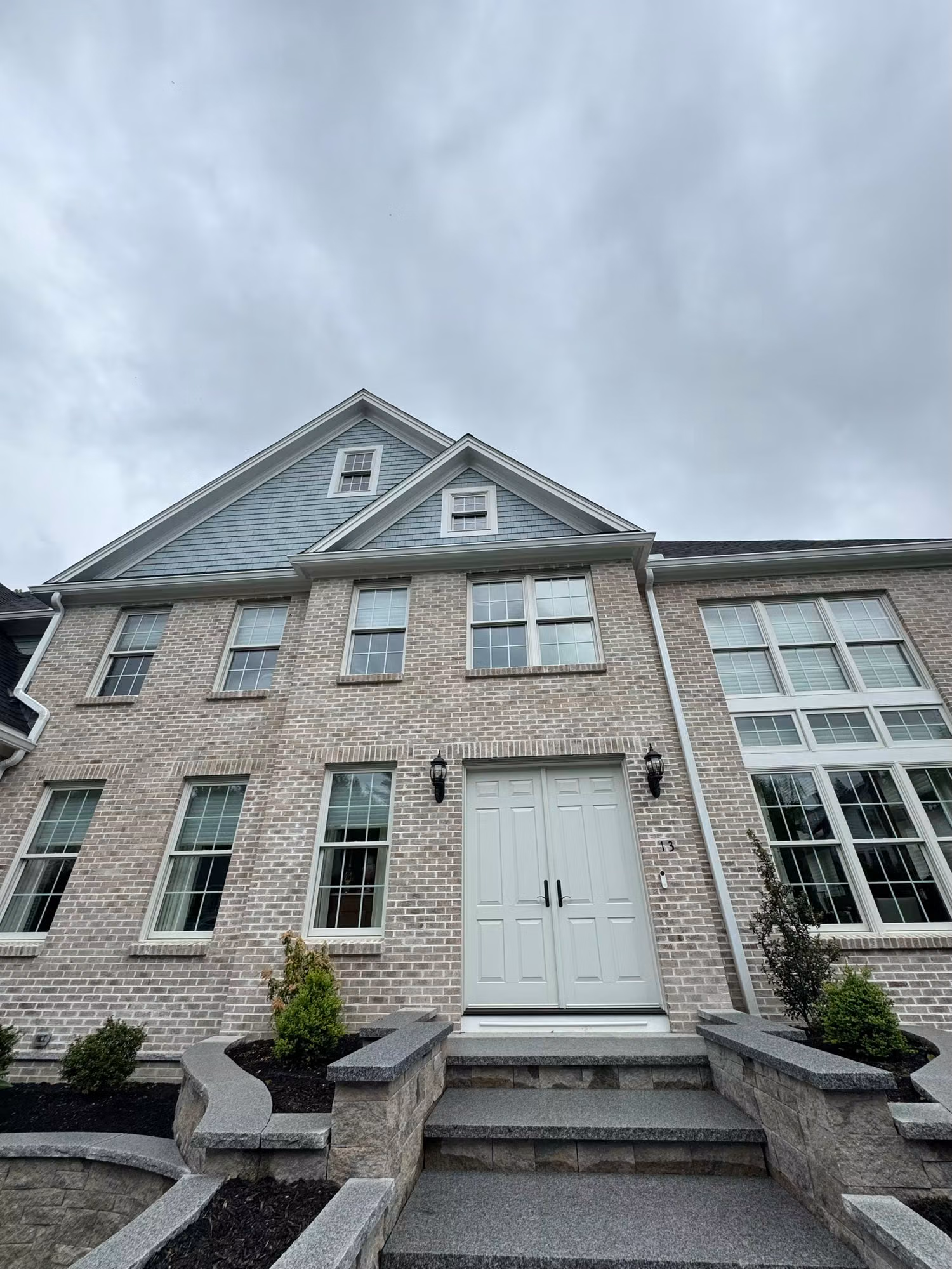 Exterior of a brick townhome facade showing multiple windows and a front entry door under an overcast sky.