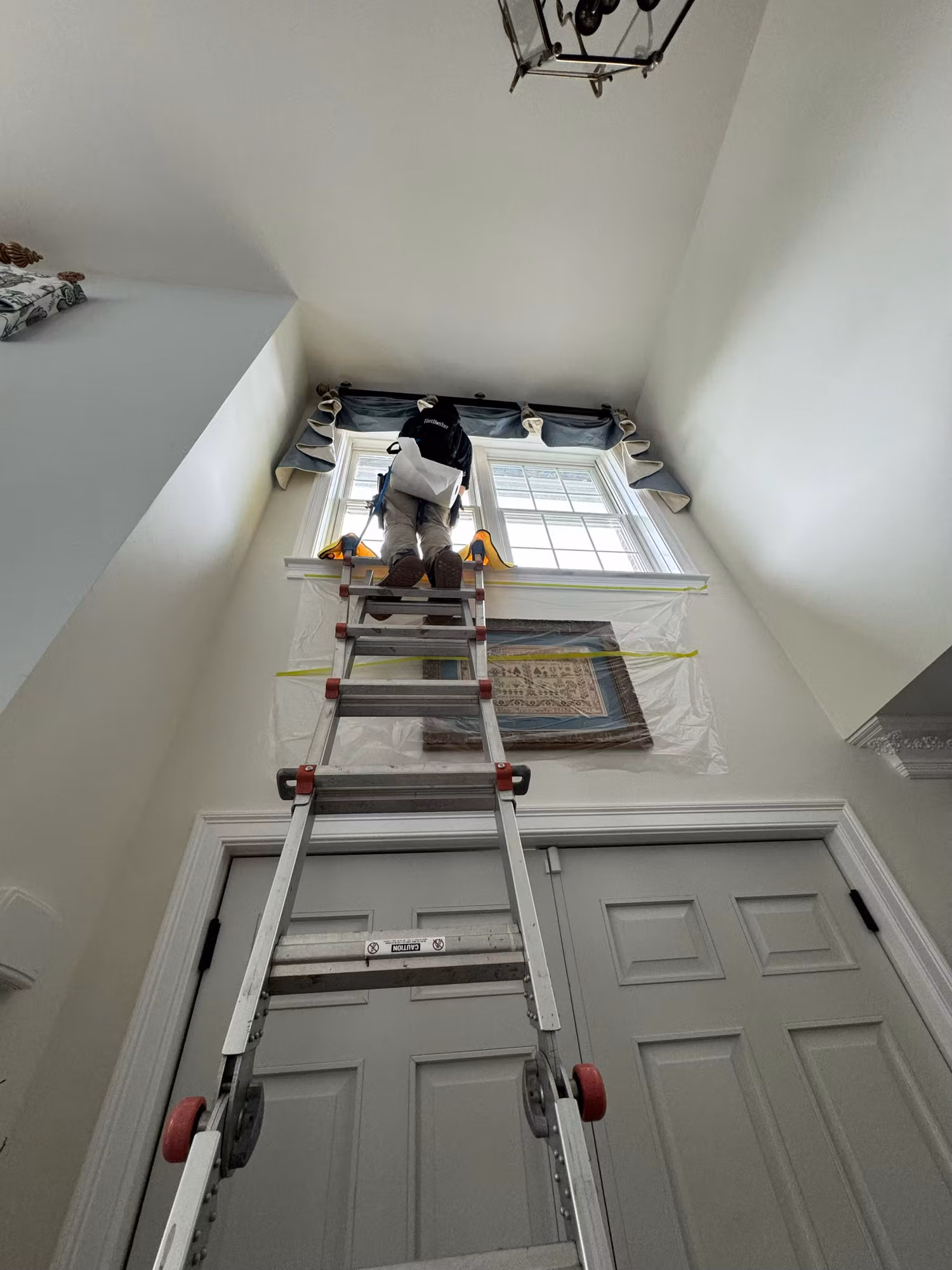 Technician on an extension ladder installing film on a high two-story stairwell window over the front door.